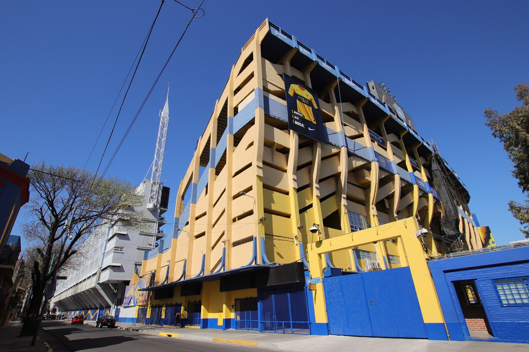 The yellow and blue exterior of La Bombonera stadium in Buenos Aires, seen from the street corner under a clear sky.