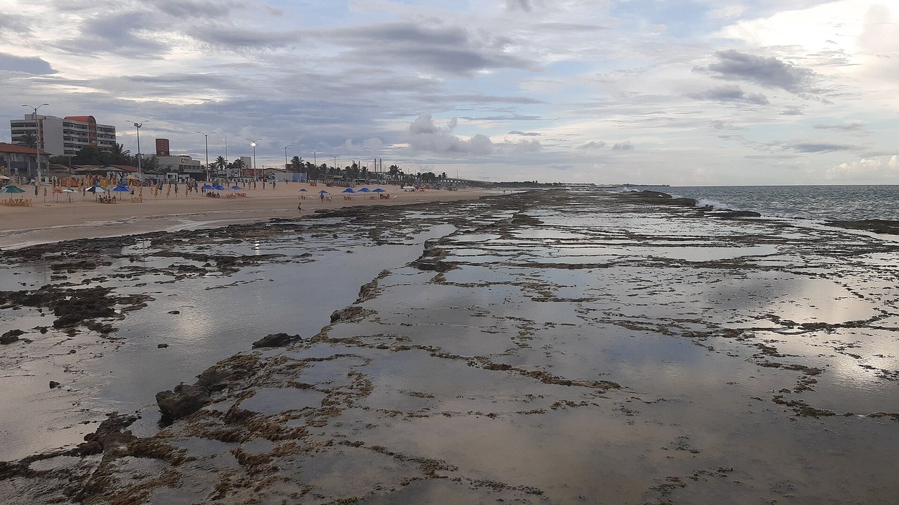 The reef and shallow pools off Praia do Meio in Natal, Brazil, with beach umbrellas and low buildings along the shore.