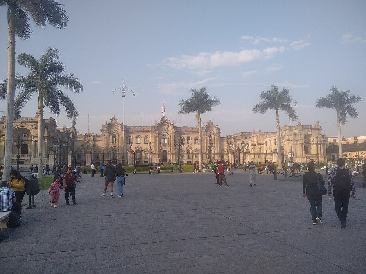 The Government Palace of Peru seen across the Plaza Mayor in Lima, with palm trees and people walking on the square