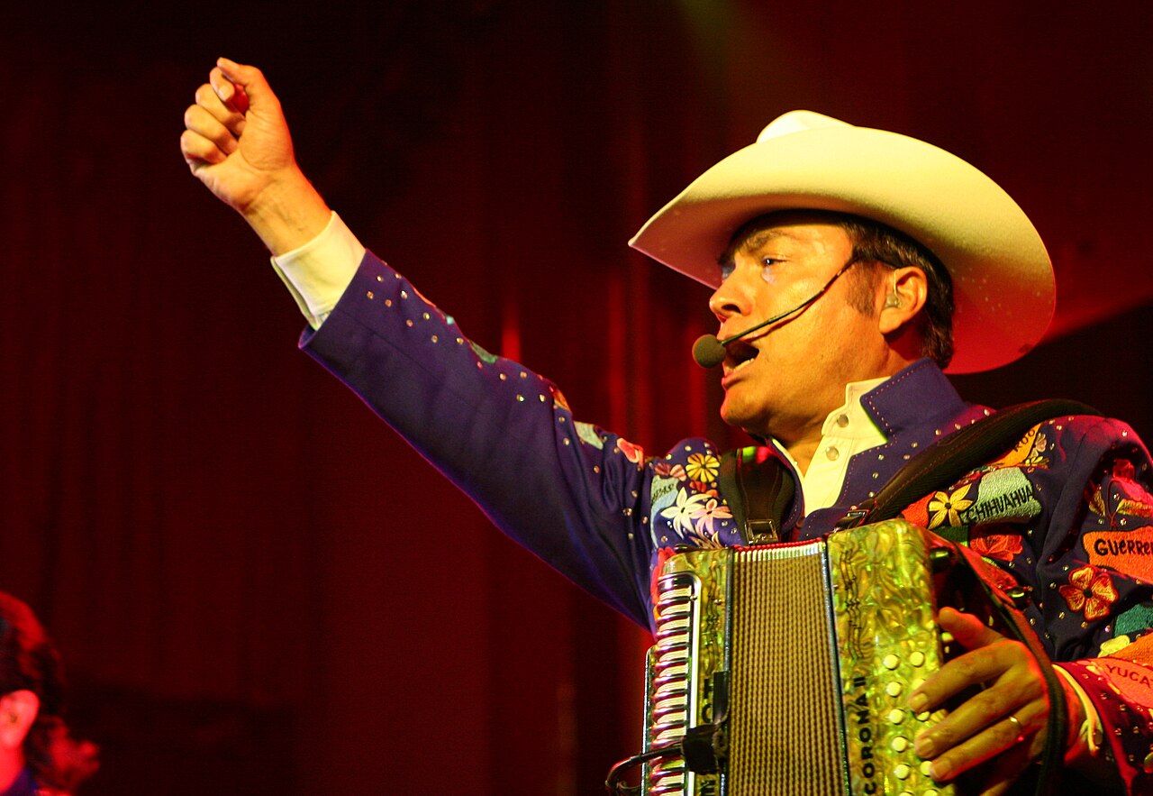 Los Tigres del Norte accordionist in a cowboy hat singing on stage, ahead of the Los Tigres del Norte Bogotá concert