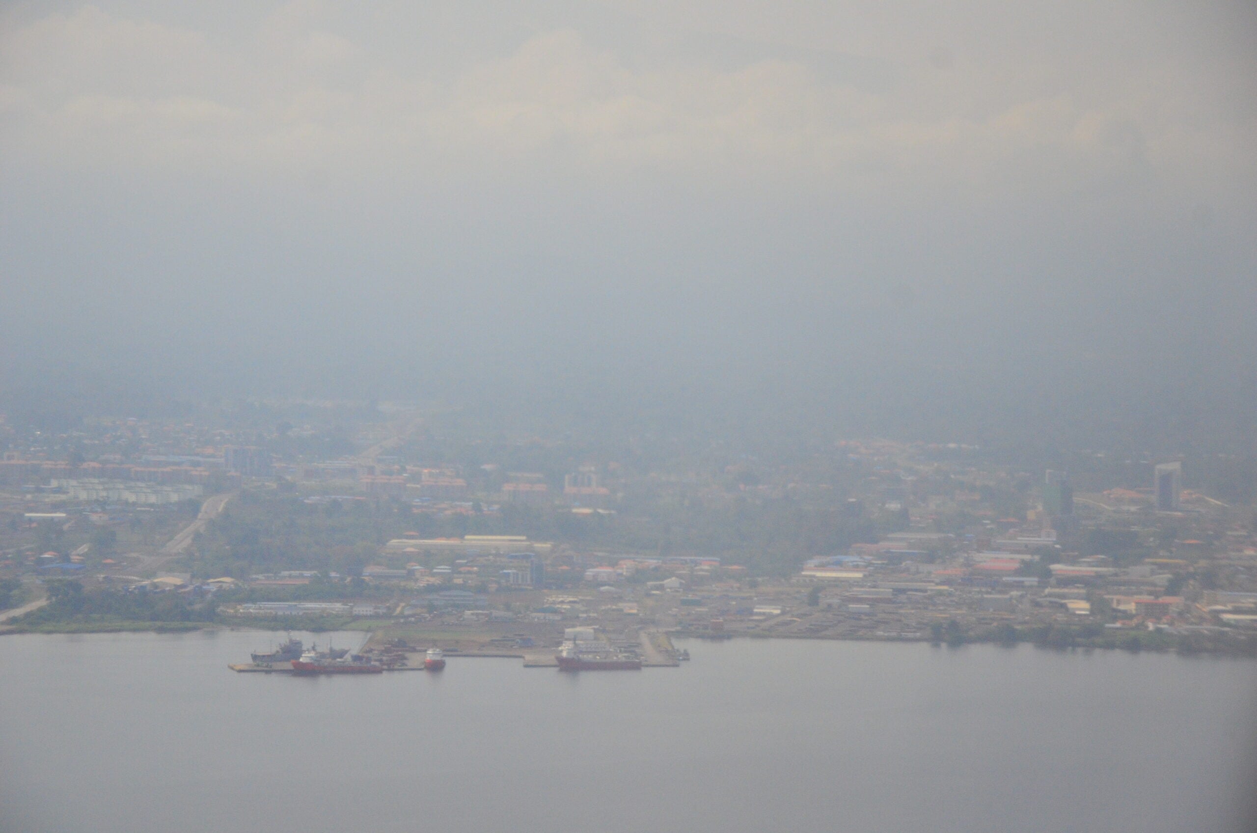 Hazy aerial view of a coastal city in Equatorial Guinea with ships moored at a pier in the foreground
