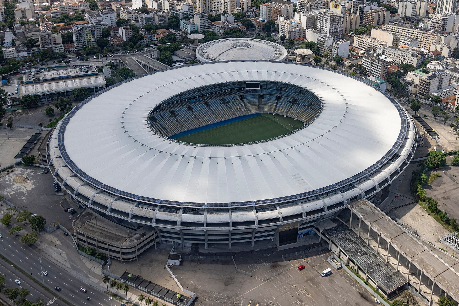Aerial view of the Maracanã stadium in Rio de Janeiro, its white roof ring surrounding the pitch, with the city around it.