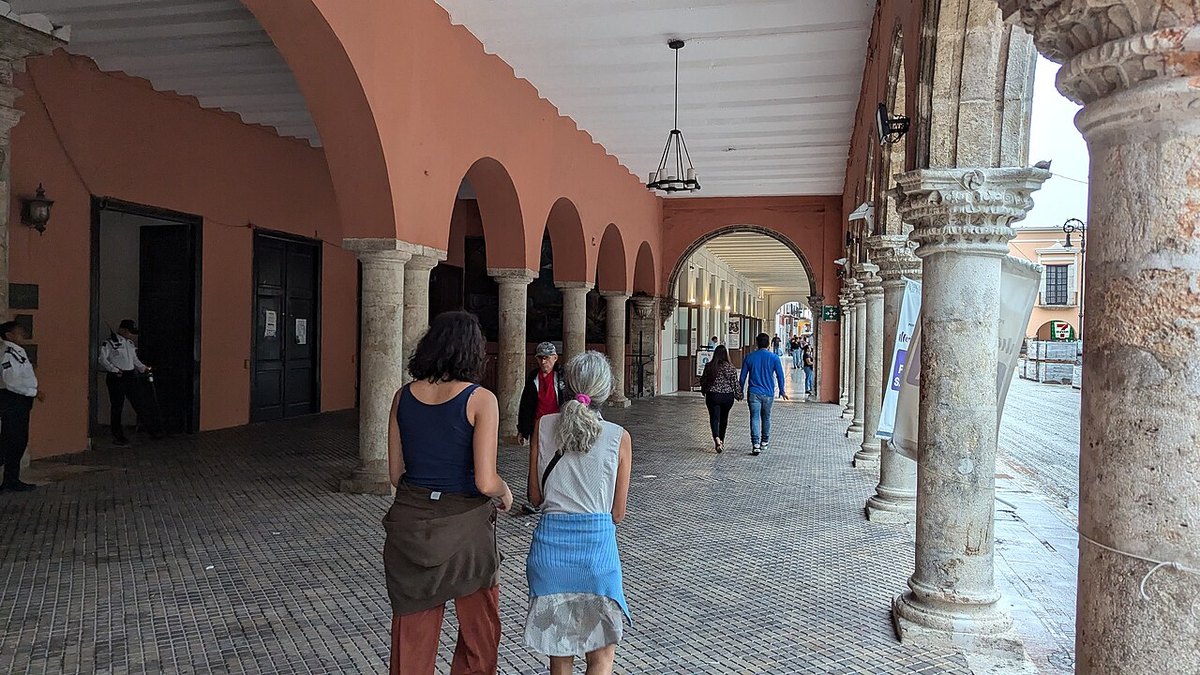 People walking under the arched colonnade beside the main square in Merida, Yucatan