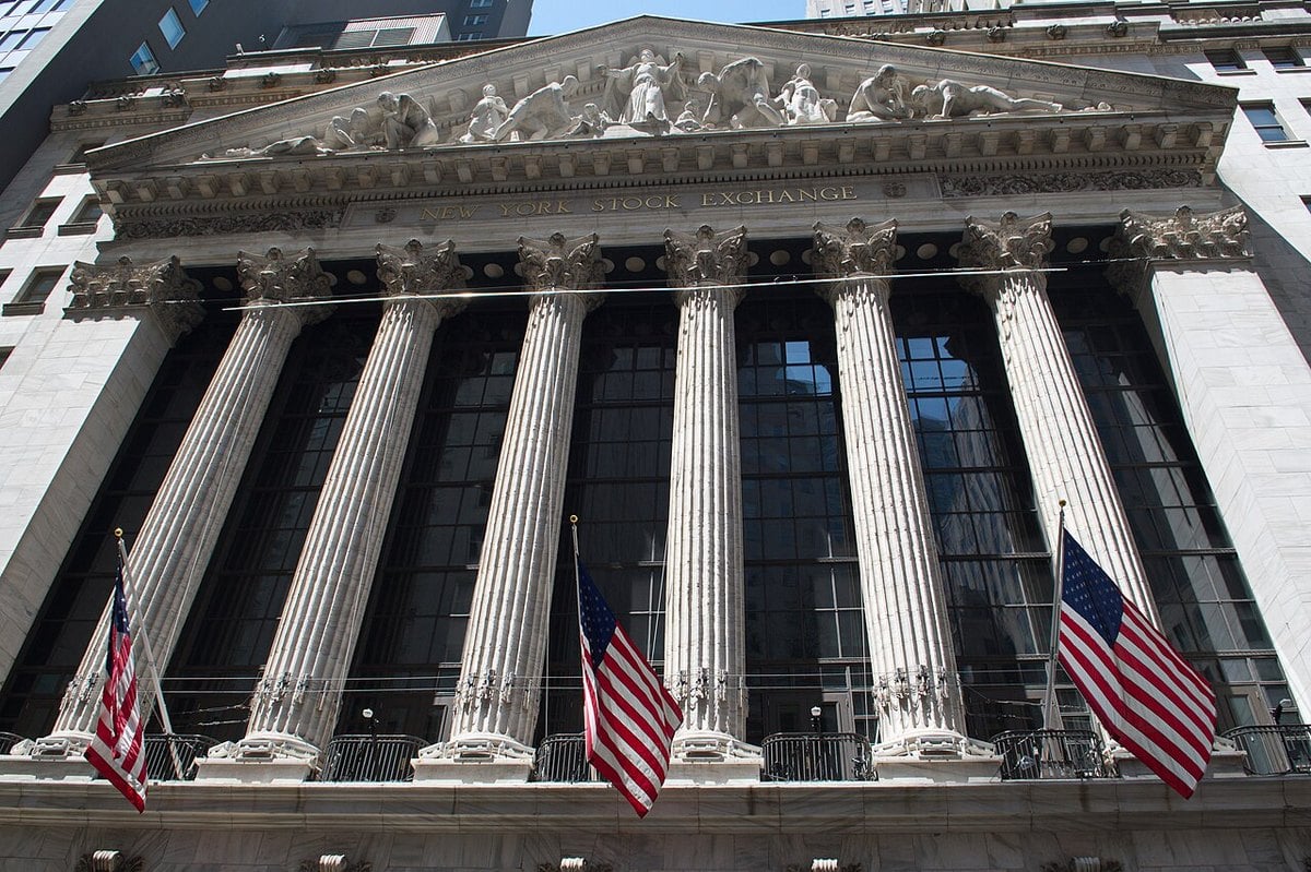 The columned facade of the New York Stock Exchange with three American flags hanging below the pediment
