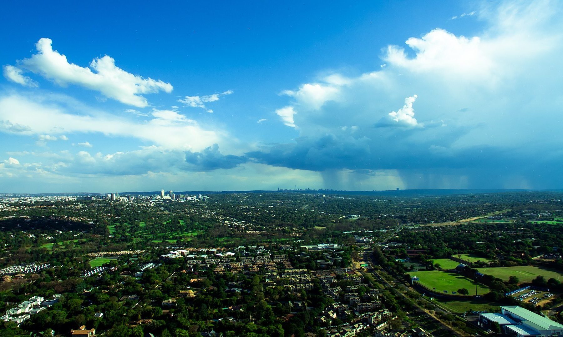 Tree-covered suburbs, sports fields and golf greens of Johannesburg, South Africa, under a summer storm, the city where Oskido Big Day Out takes place at Huddle Park on 28 November 2026