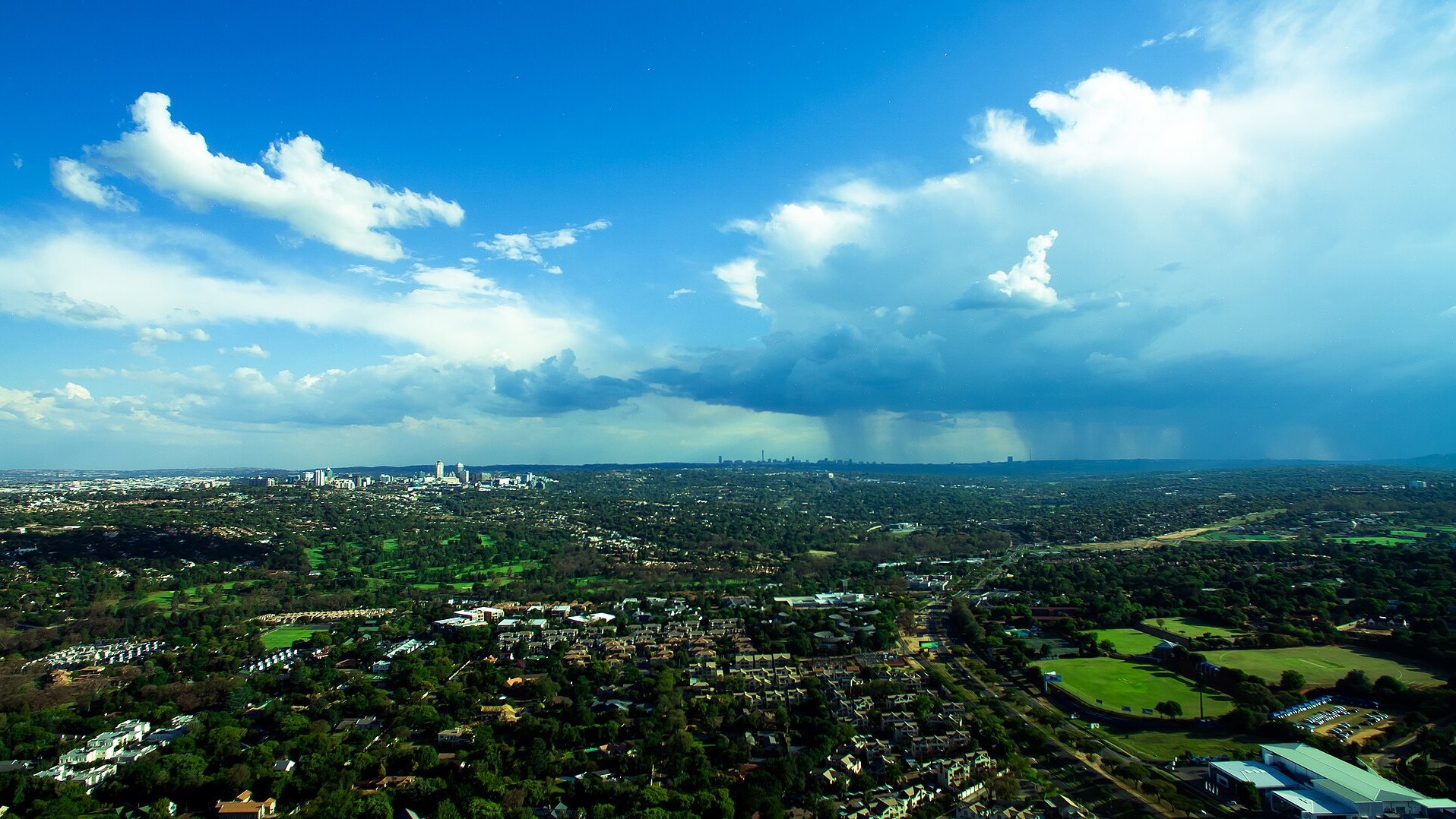 Tree-covered suburbs, sports fields and golf greens of Johannesburg, South Africa, under a summer storm, the city where Oskido Big Day Out takes place at Huddle Park on 28 November 2026