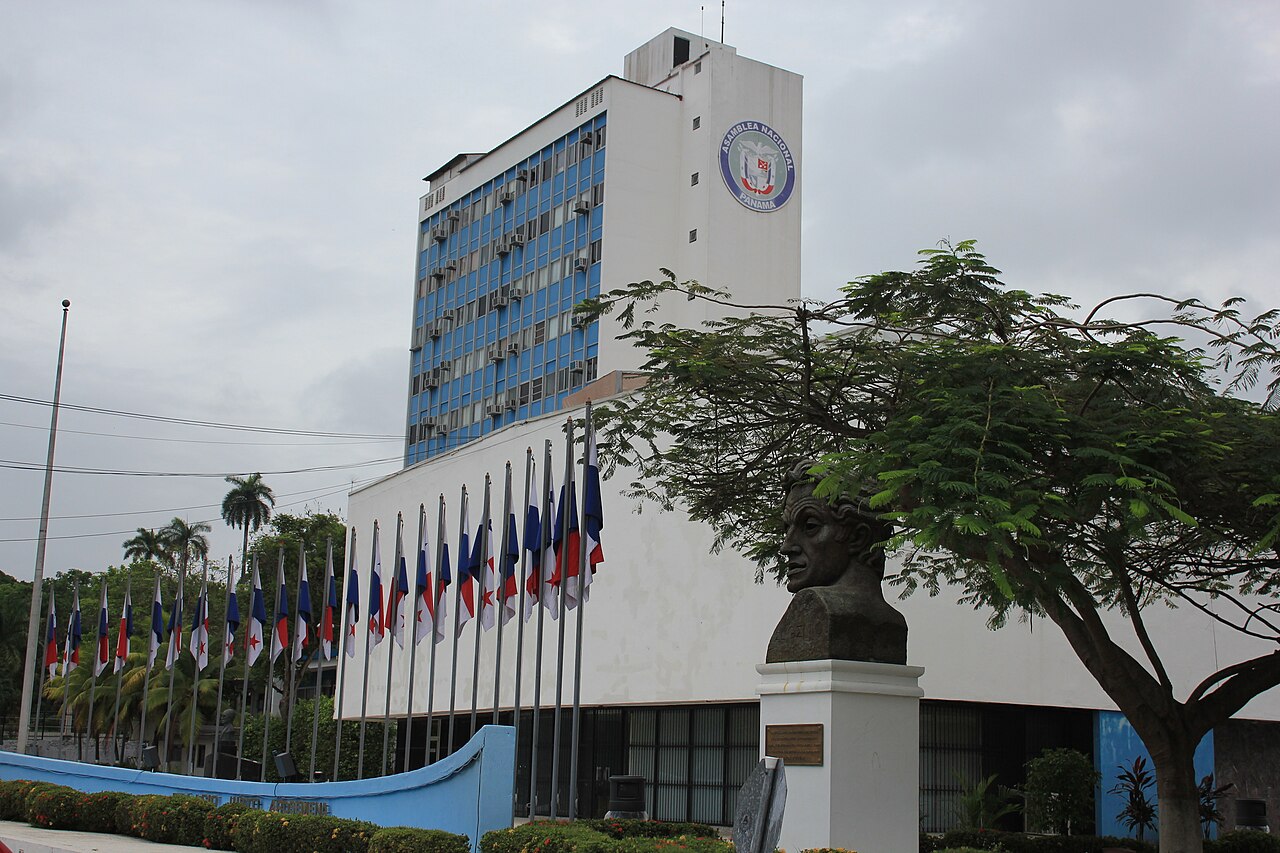 The National Assembly building in Panama City with its logo, a row of Panamanian flags and a bronze bust in front; Panama electoral reform goes to the full Assembly