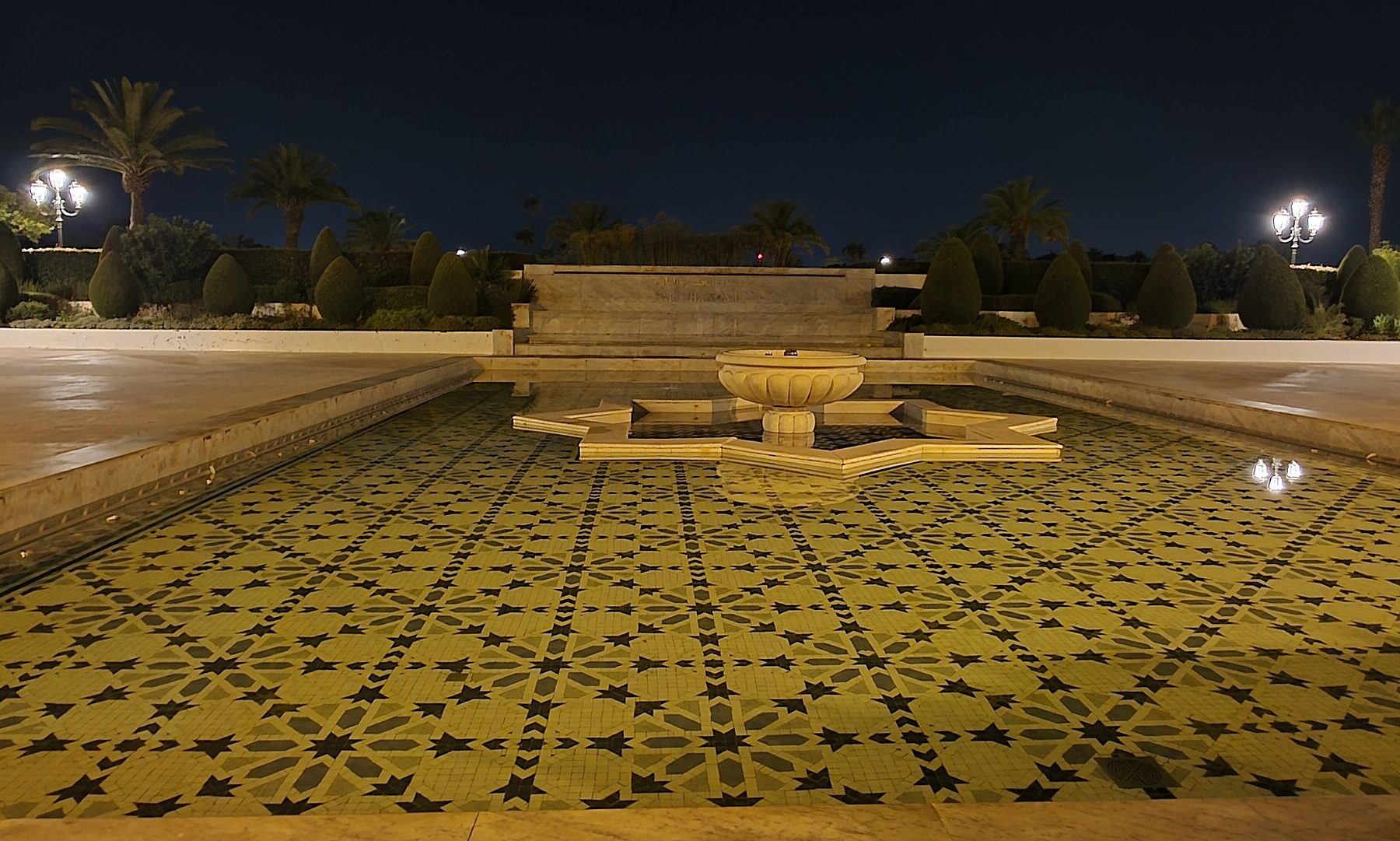 The reflecting pool at the Parc Hassan II in Rabat at night, its floor patterned with black and gold zellij stars around a fountain.