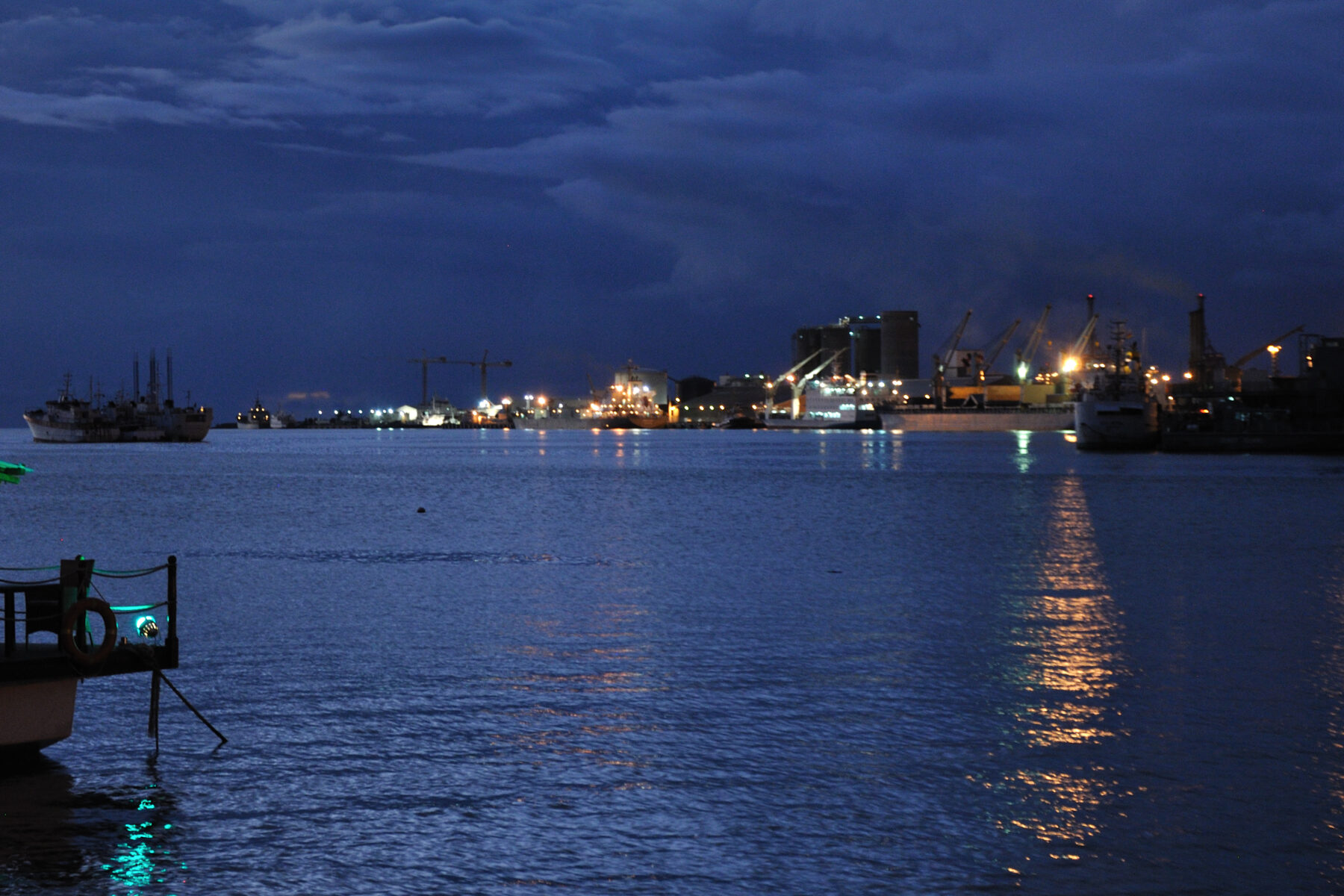 Port Louis harbour in Mauritius at dusk, with lit cranes, silos and ships across calm water