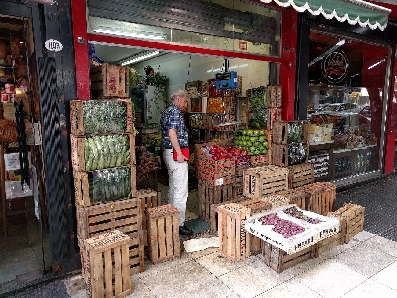 A man looking at crates of vegetables and fruit outside a small greengrocer in Buenos Aires