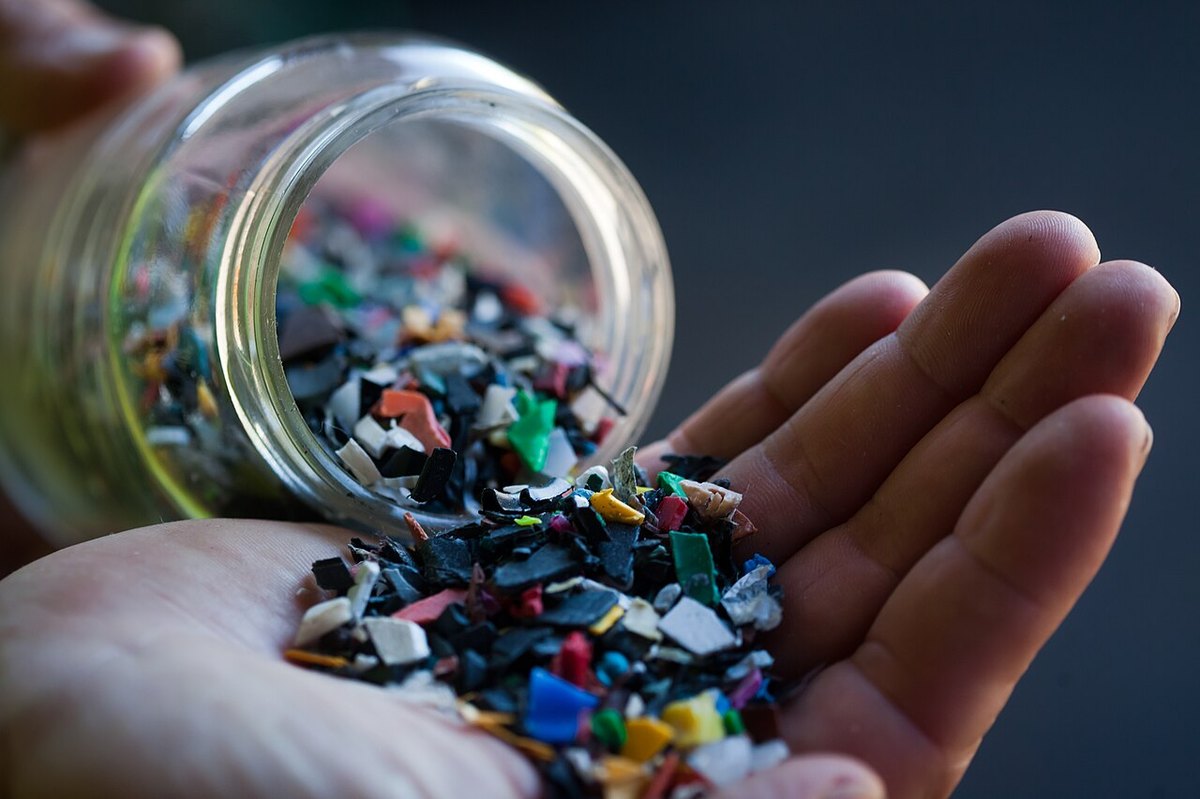 A hand holding recycled plastic flakes poured from a glass jar at a Brazilian processing site