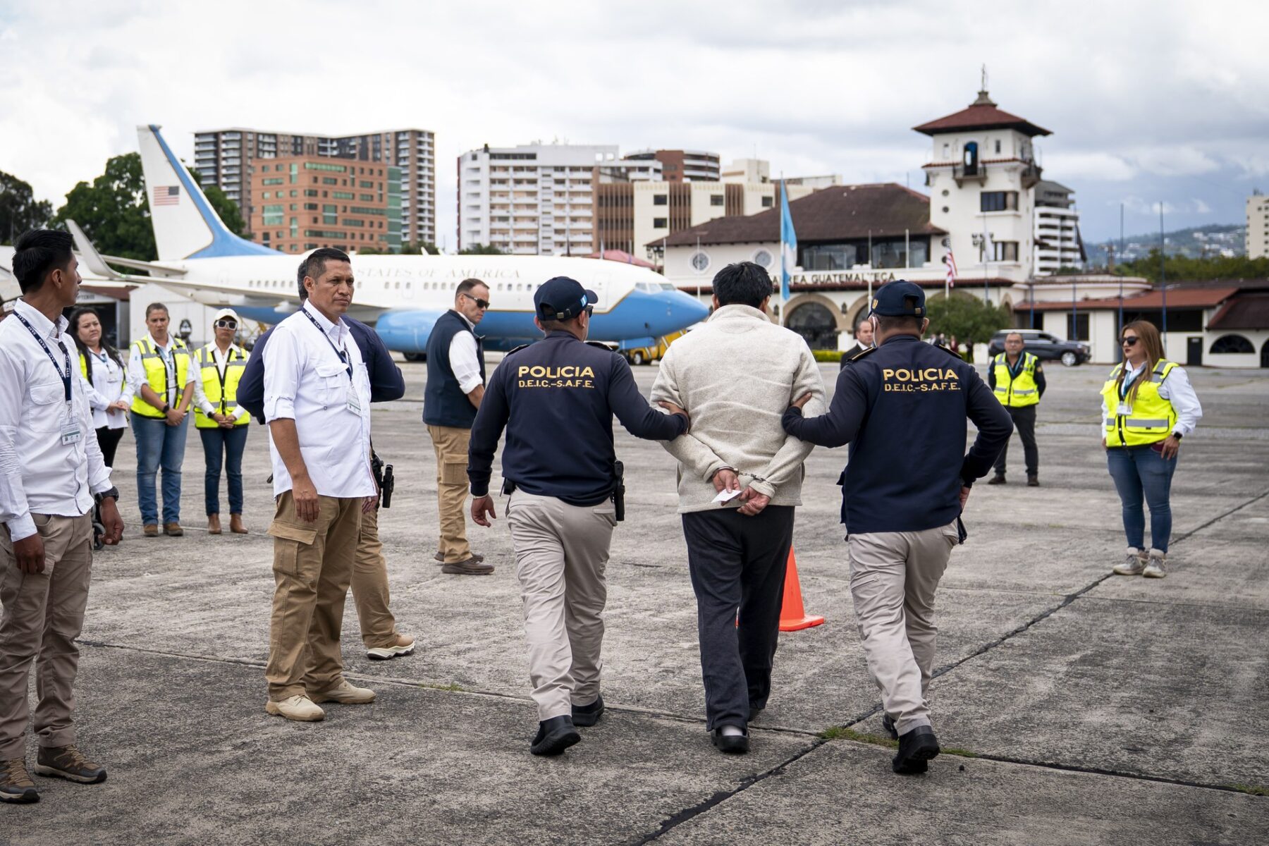 Guatemalan police escort a handcuffed man at La Aurora airport as a US government aircraft stands by