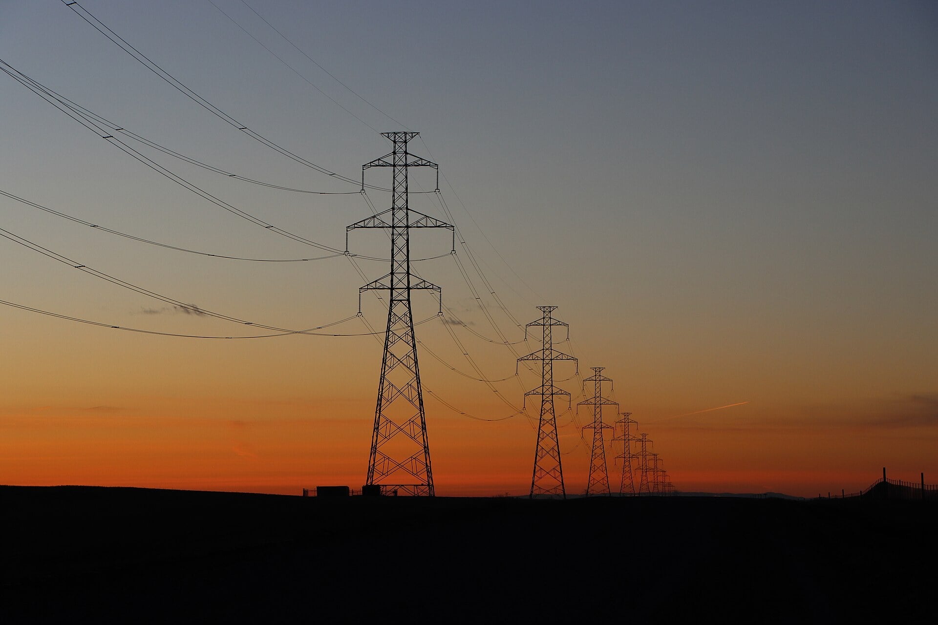 High-voltage electricity transmission lines and pylons silhouetted at dusk