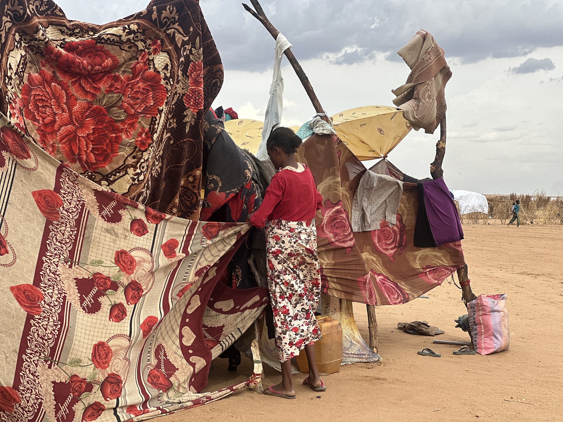 A displaced Sudanese woman with only pieces of cloth for shelter