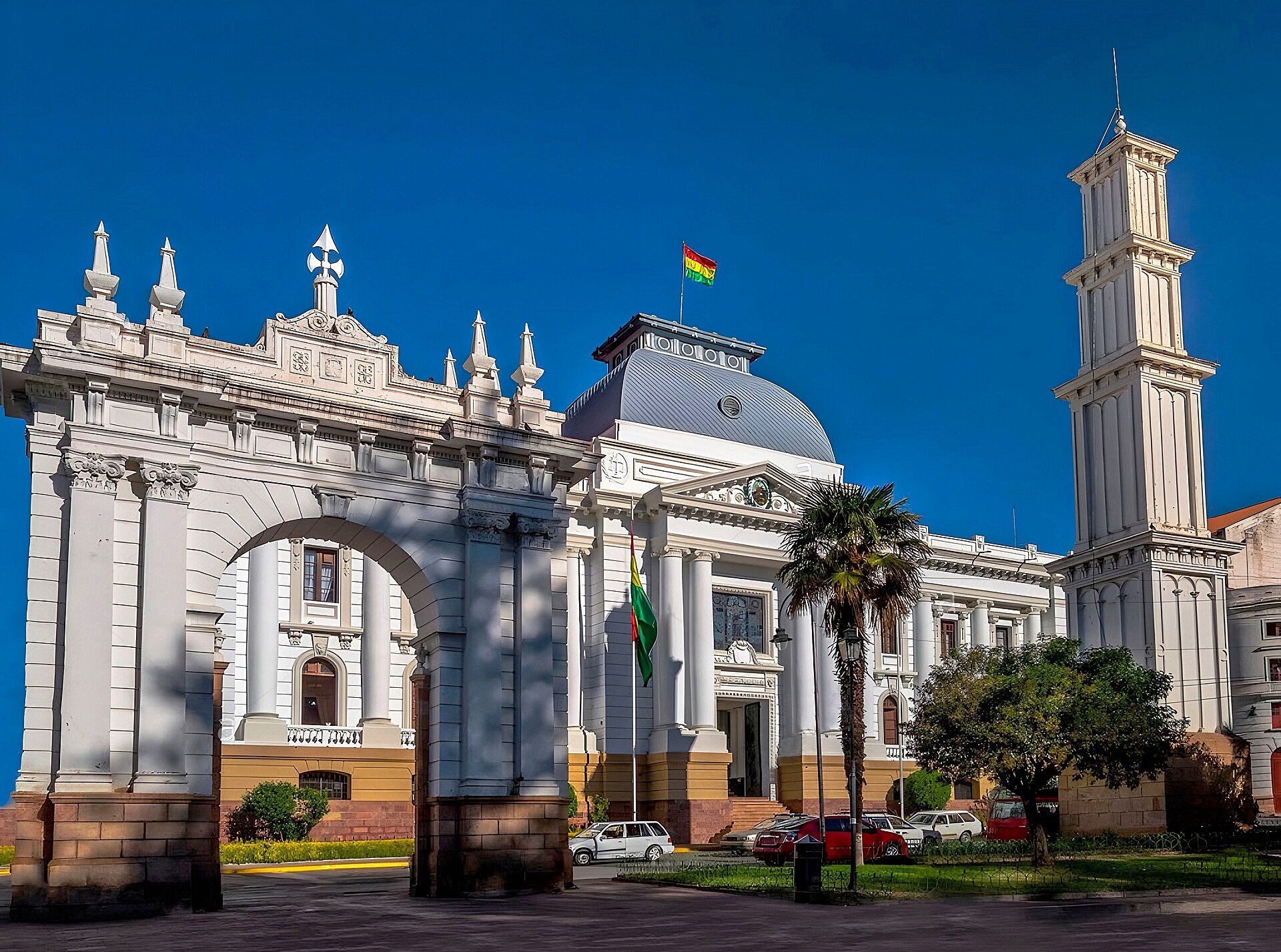 White neoclassical palace of justice behind a stone arch in Sucre, Bolivia, with the national flag flying