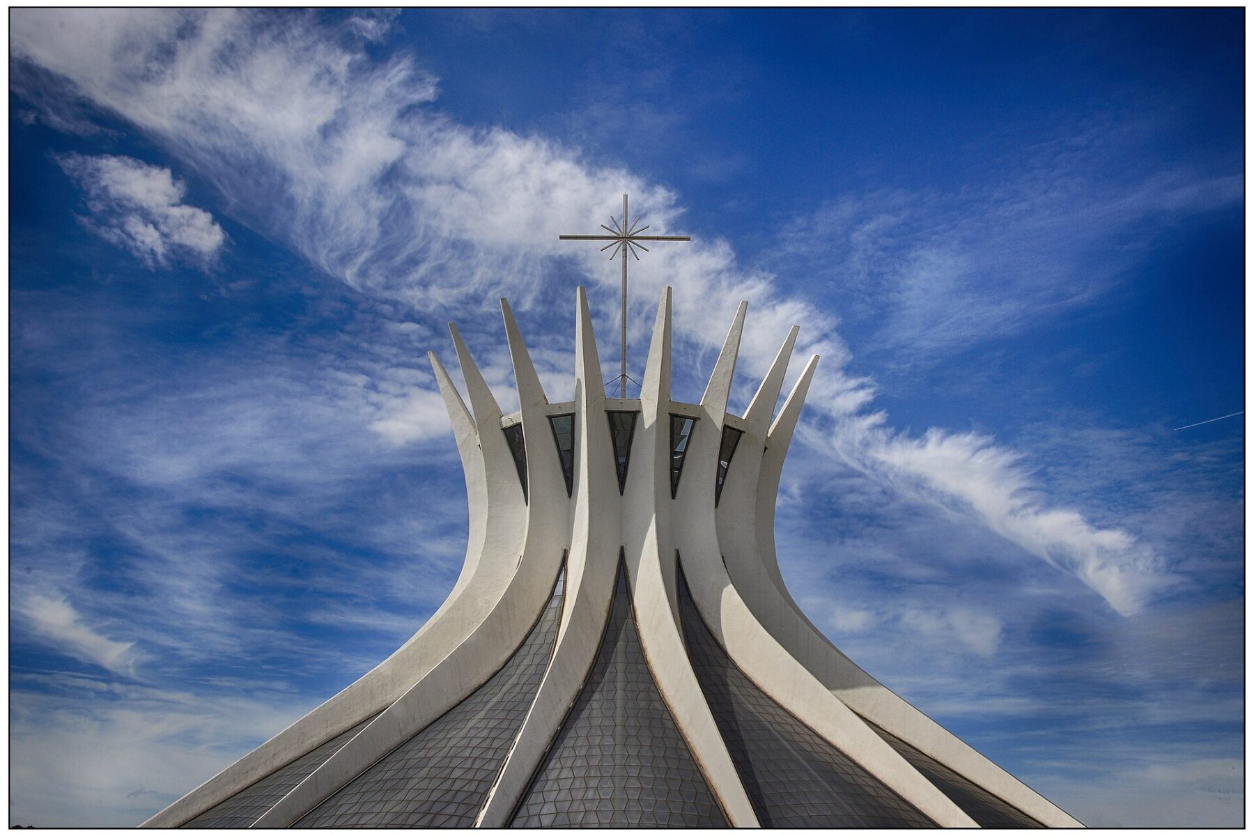 Curved concrete columns and cross of the Metropolitan Cathedral of Brasília against a blue sky