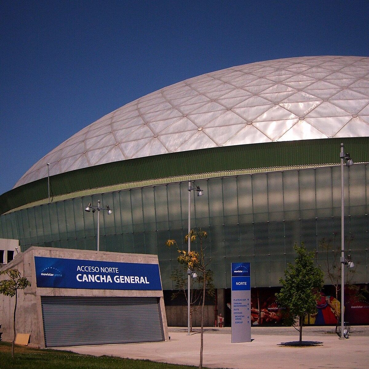 The white domed roof and glass facade of the arena in Parque O Higgins, Santiago, with Movistar Arena signage at the north entrance