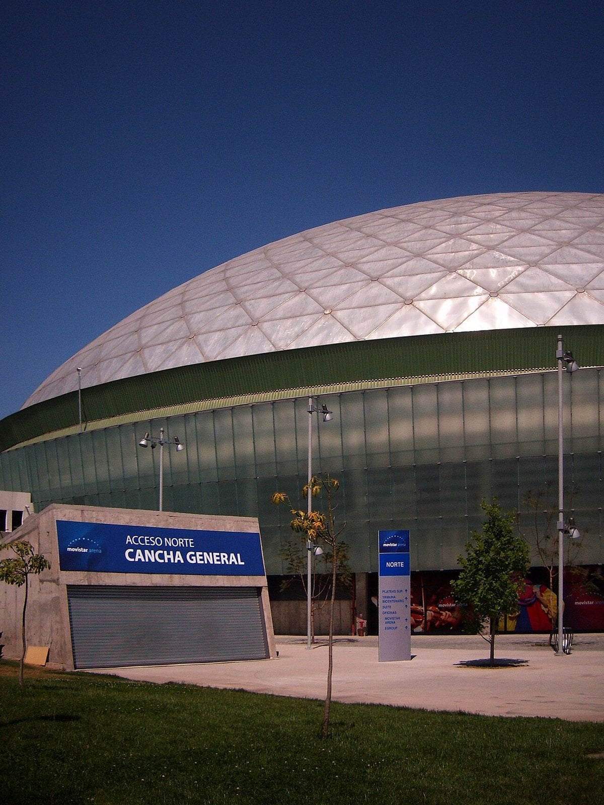 The white domed roof and glass facade of the arena in Parque O Higgins, Santiago, with Movistar Arena signage at the north entrance