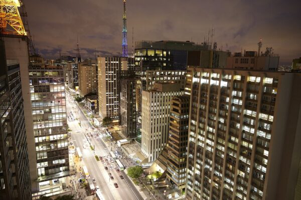 São Paulo nightlife: Avenida Paulista at night seen from above, with lit office towers, traffic and a floodlit broadcast mast