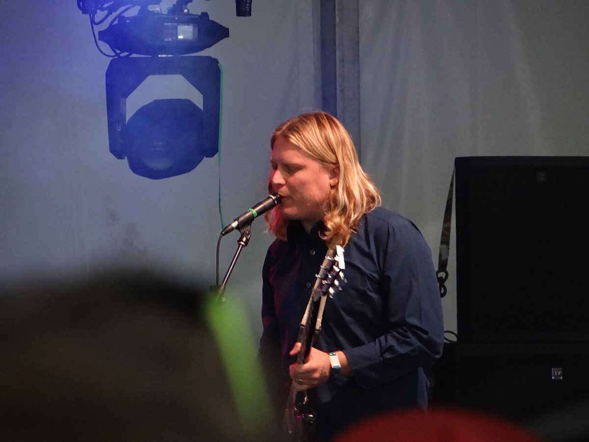 Ty Segall singing into a microphone with a guitar, under blue stage light
