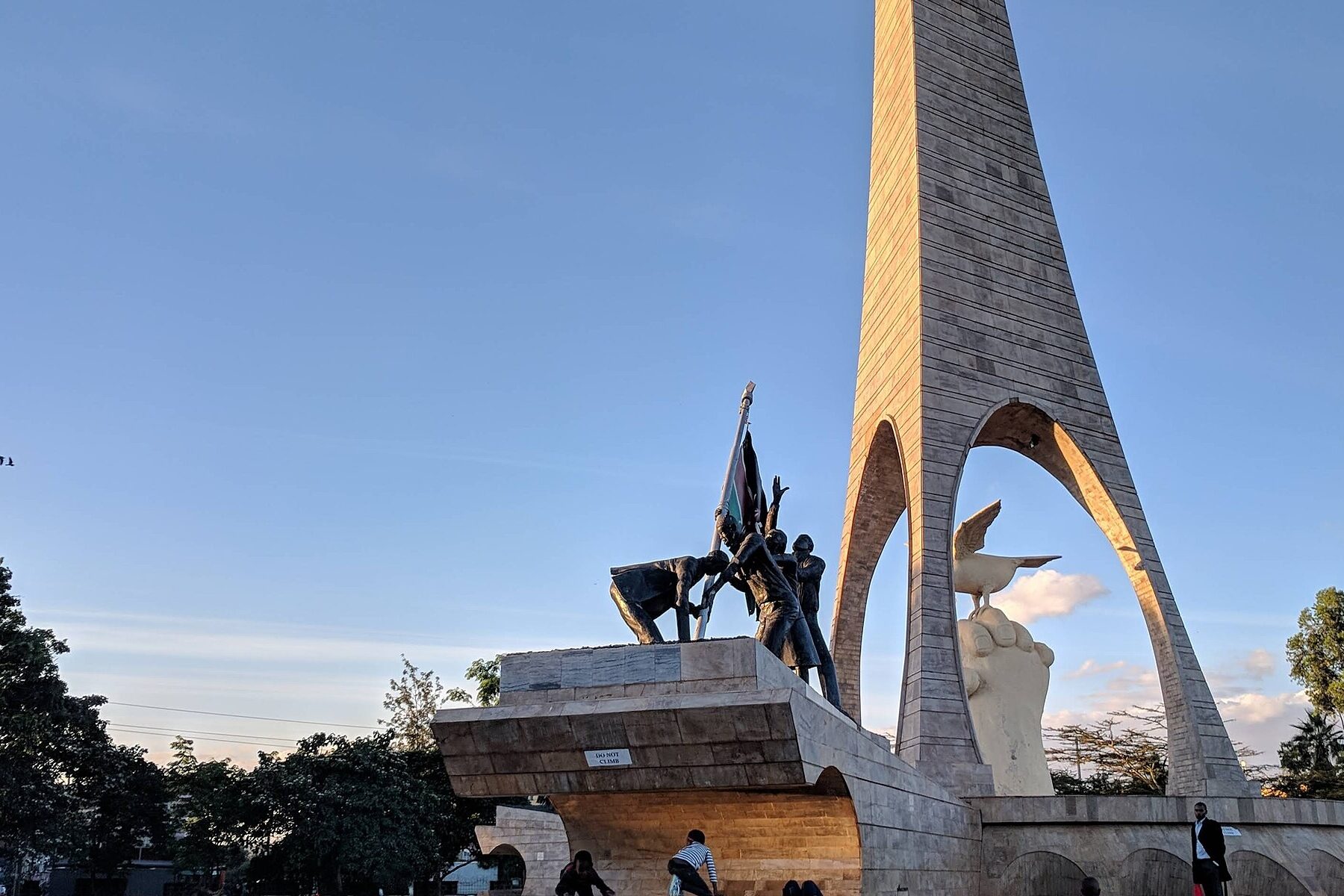 The tall stone monument at Uhuru Gardens in Nairobi, with a bronze group raising the Kenyan flag and a dove sculpture beside it.