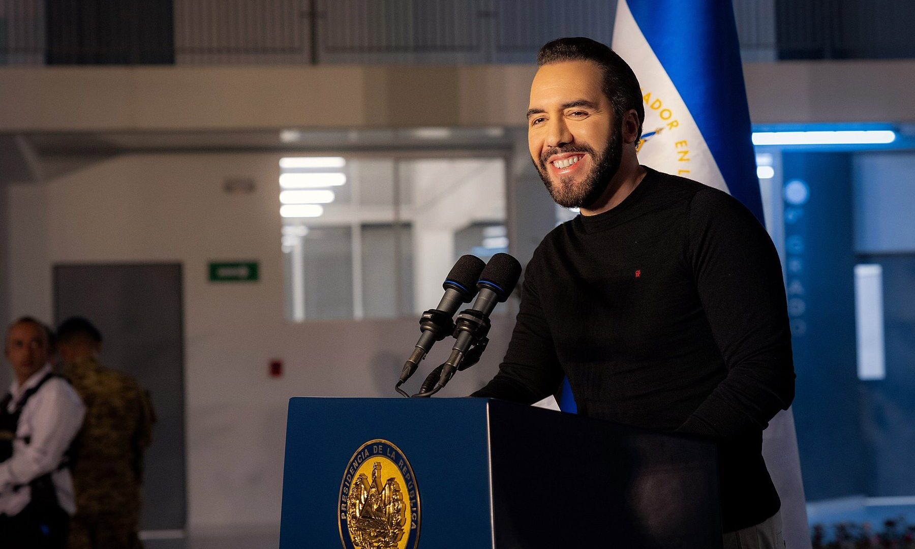Salvadoran President Nayib Bukele speaking at a podium in front of the Salvadoran flag in Juayúa