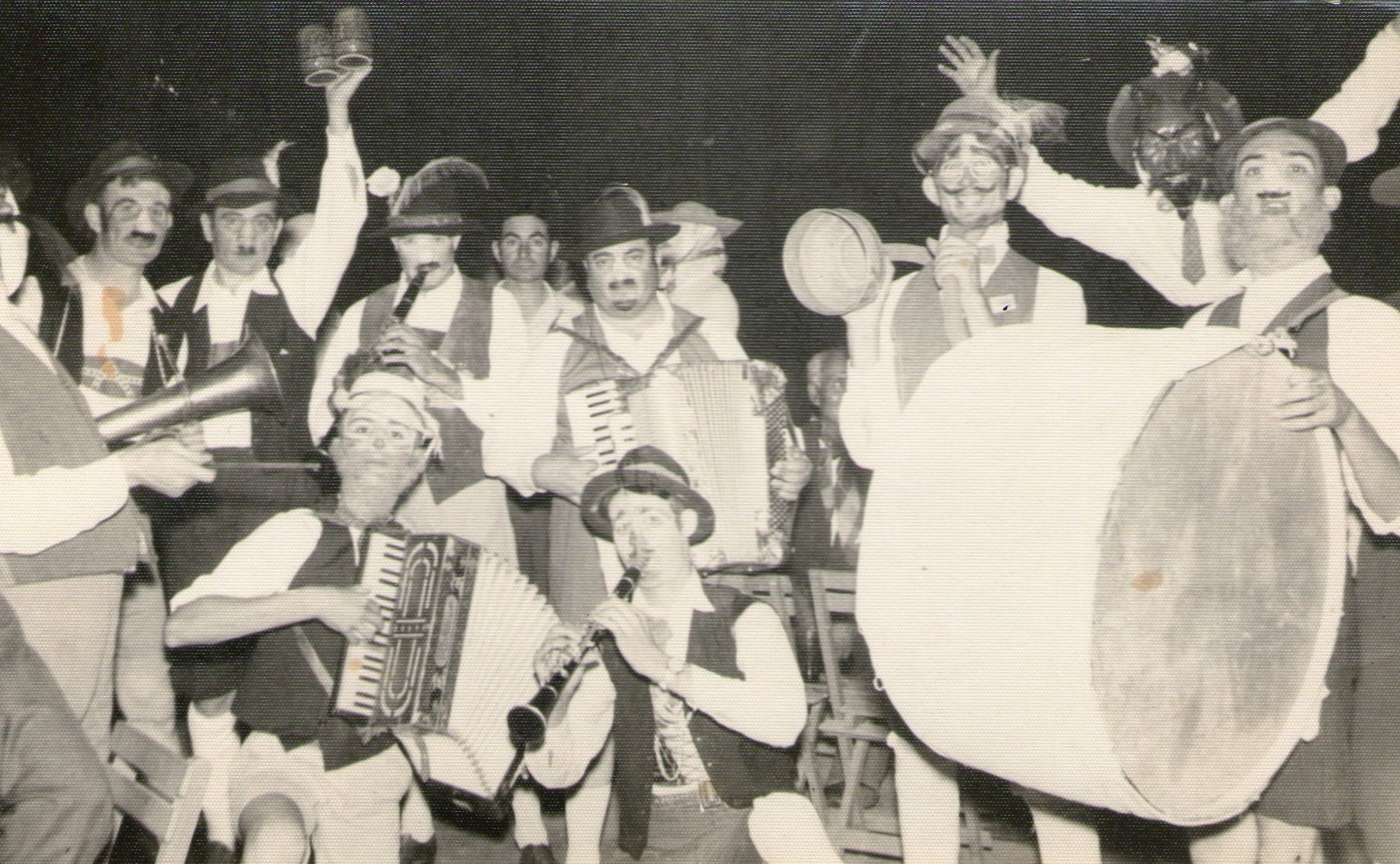 Black and white archive photograph of a band in Tyrolean hats with accordions, a clarinet, a drum and raised beer mugs.