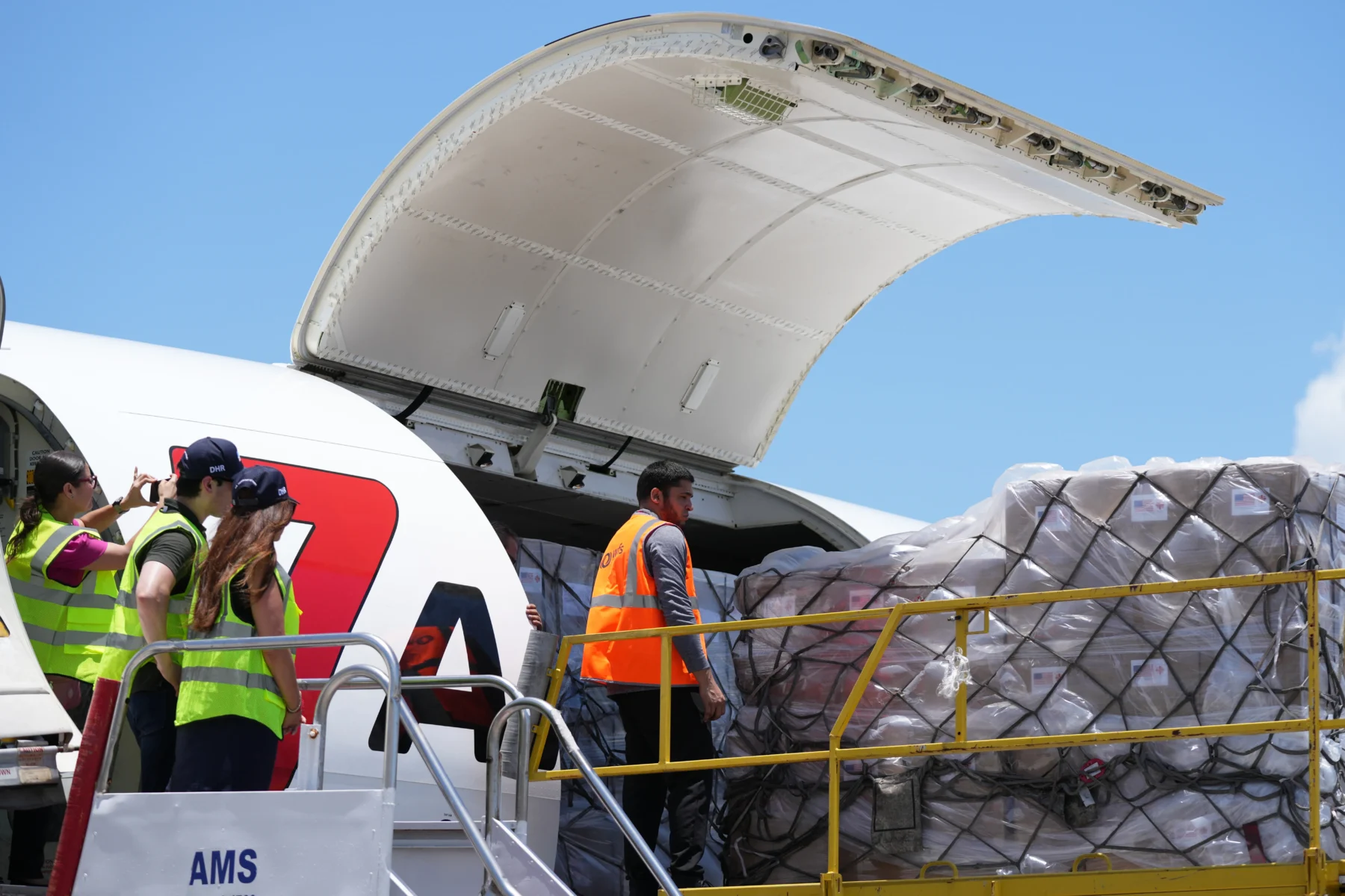 Pallets of aid boxes with US flag labels being unloaded from a cargo aircraft