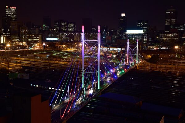 Nelson Mandela Bridge lit up at night with the Johannesburg skyline behind