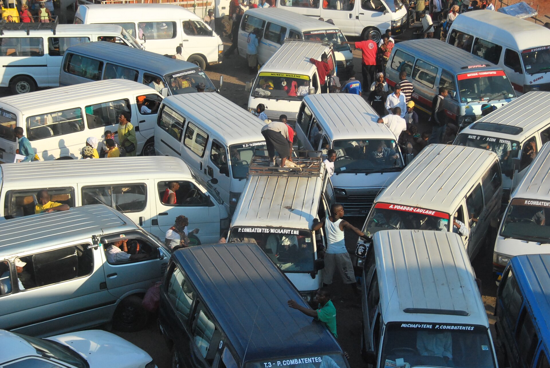 Crowded chapa minibus terminal in Maputo, Mozambique, with dozens of white minibuses and passengers