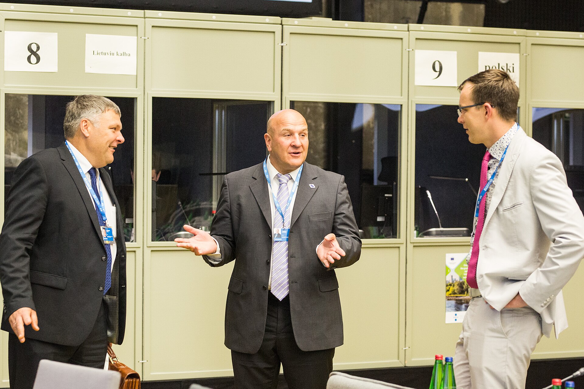 Three men in suits talk in front of interpreter booths at an energy policy conference in Tallinn