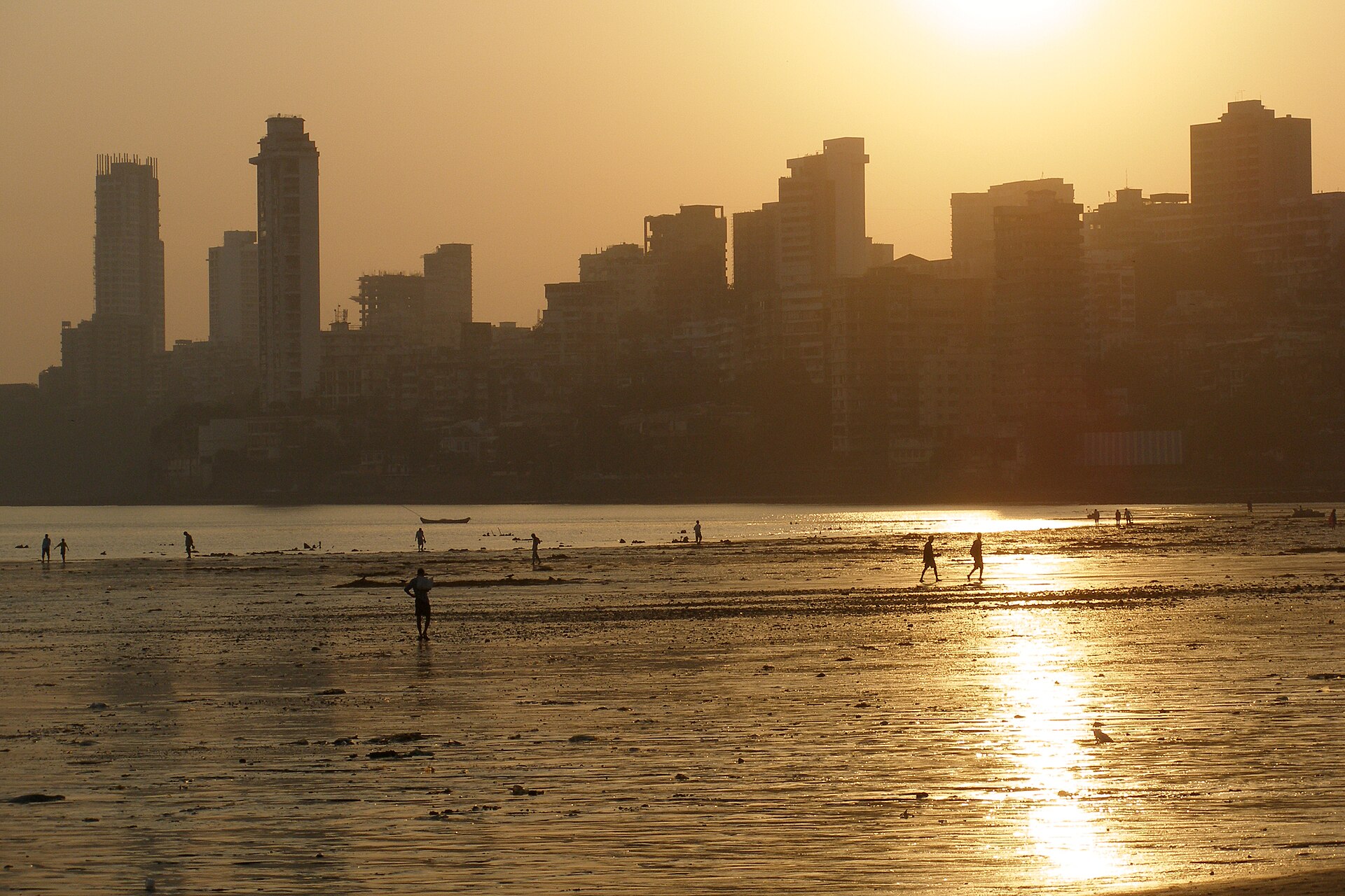 Mumbai high-rises silhouetted against a golden sunset above a tidal beach