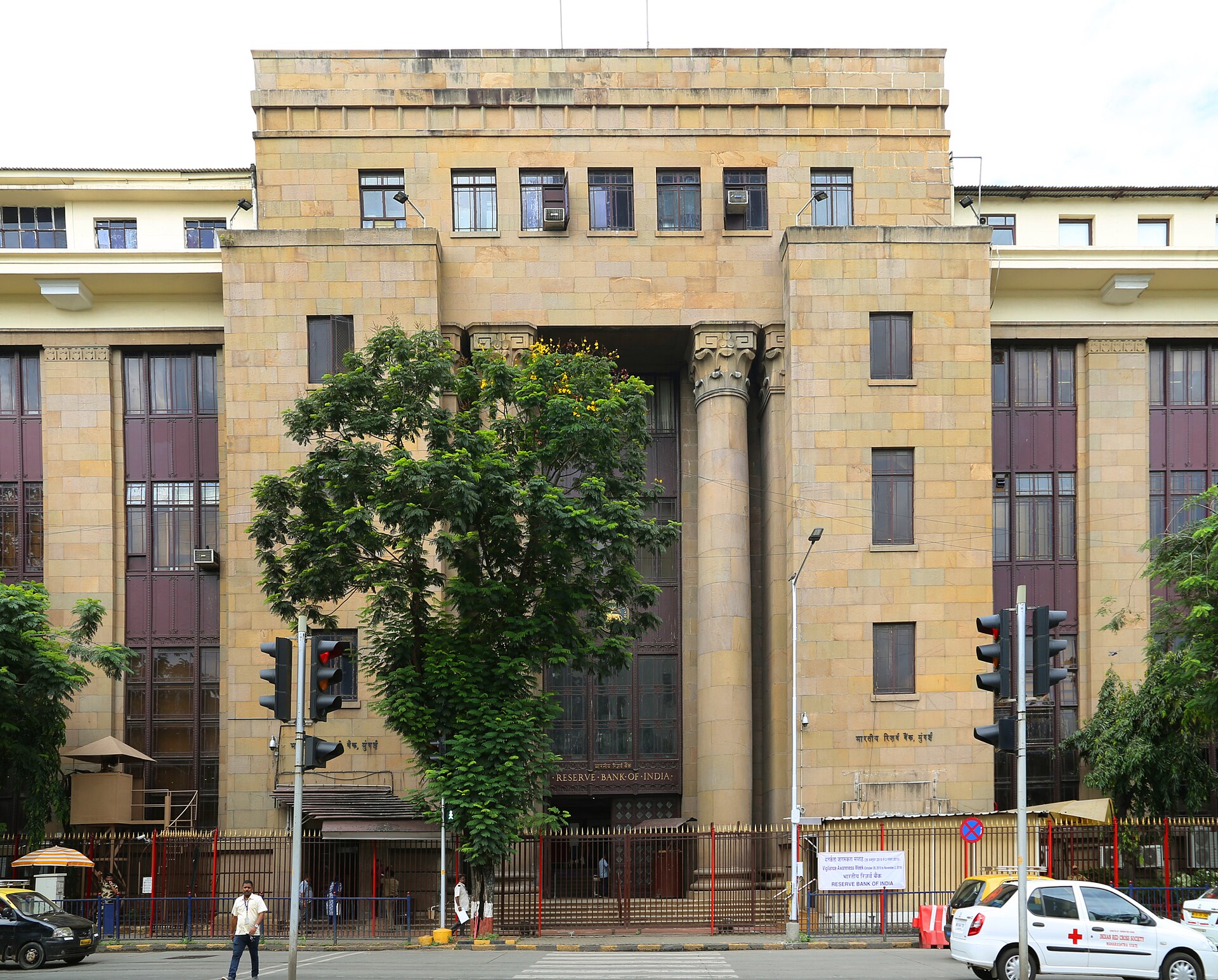 Front entrance of the Reserve Bank of India building in Mumbai with a tree and traffic lights in front.