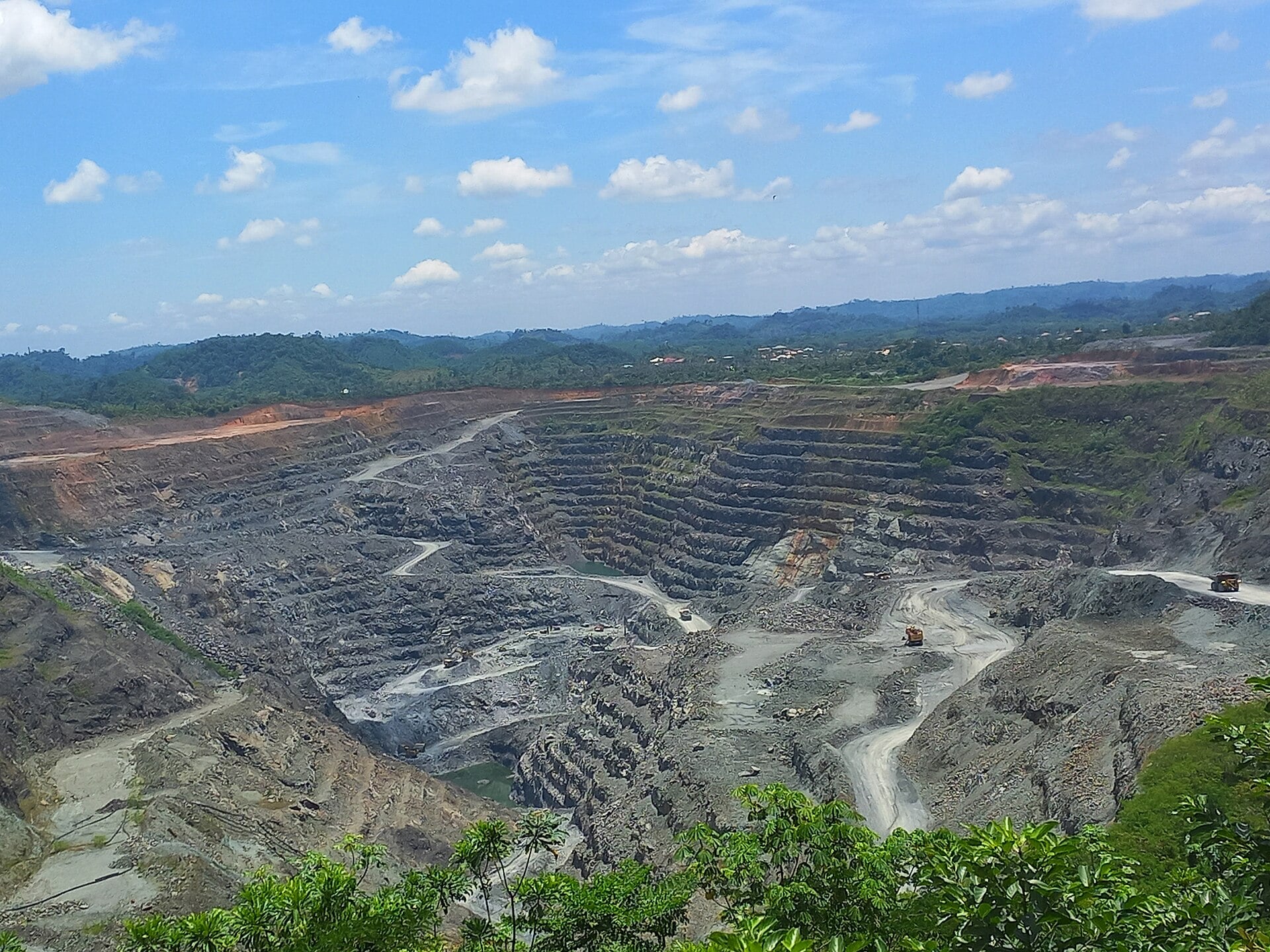 Open-pit manganese mine at Nsuta in Ghana with terraced benches and haul trucks under a blue sky