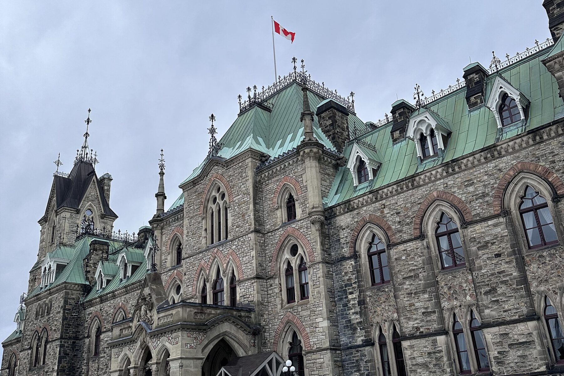 A stone government building on Parliament Hill in Ottawa with a Canadian flag