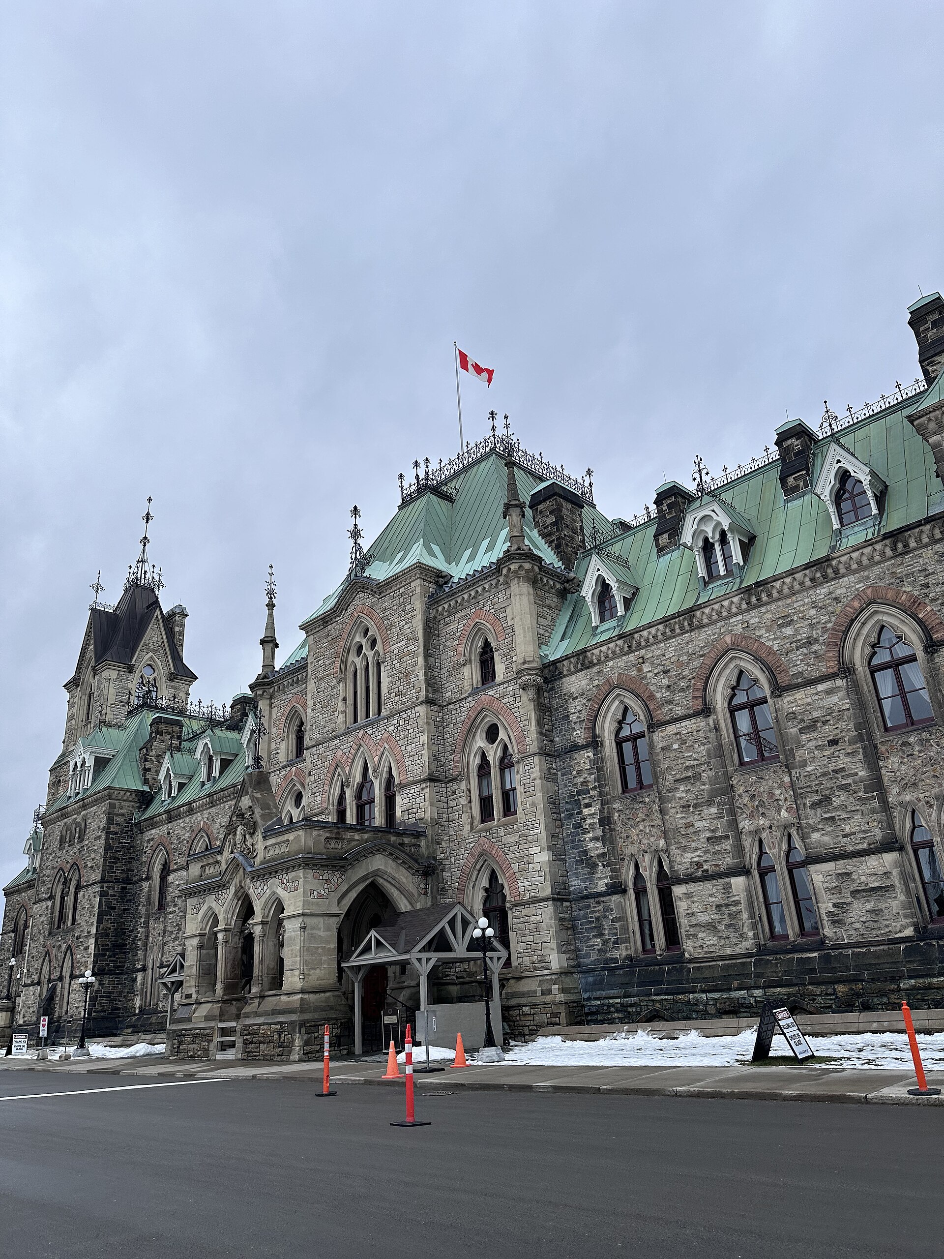 A stone government building on Parliament Hill in Ottawa with a Canadian flag