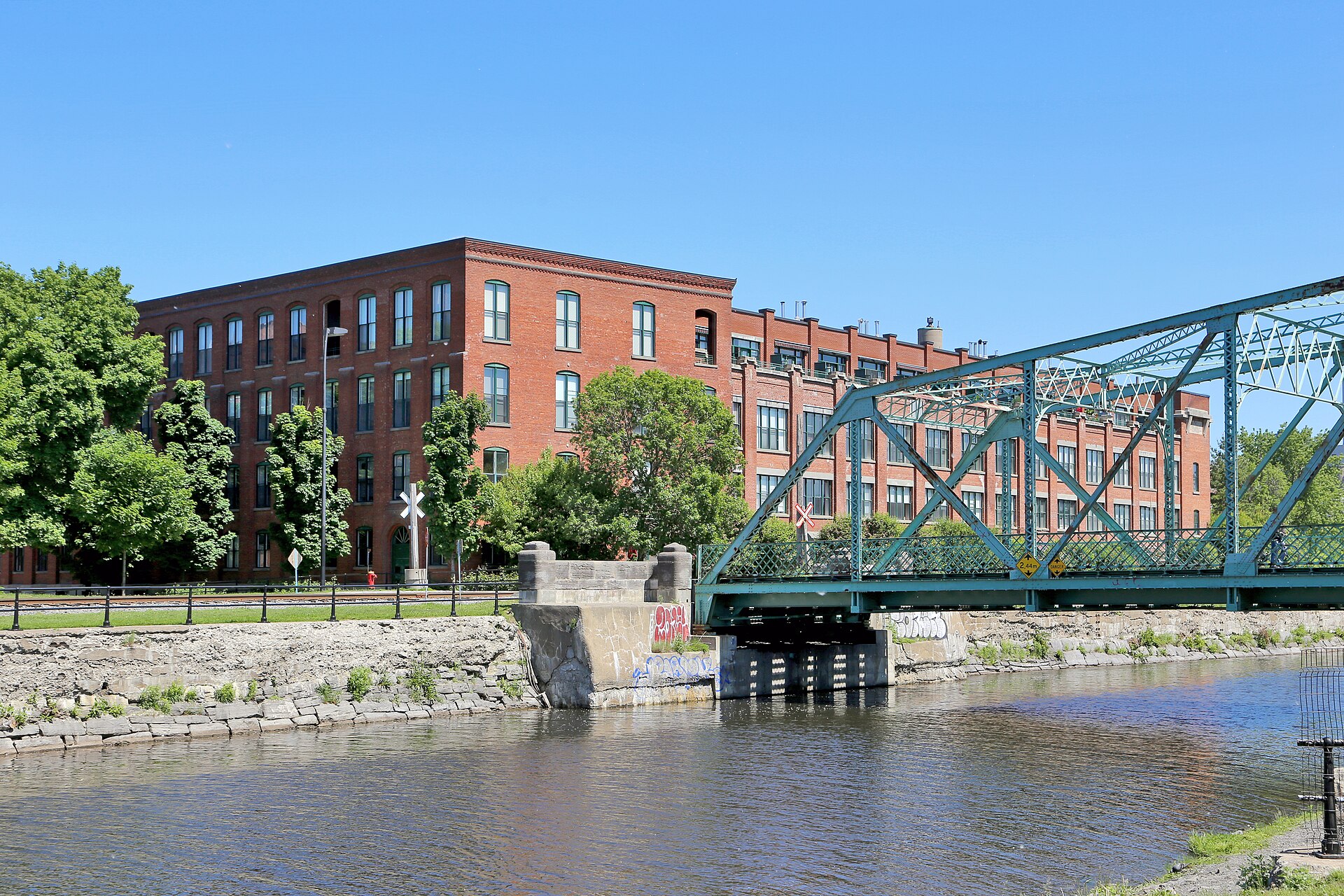 Stelco rolling mill building in Montreal next to a green steel bridge over the canal.
