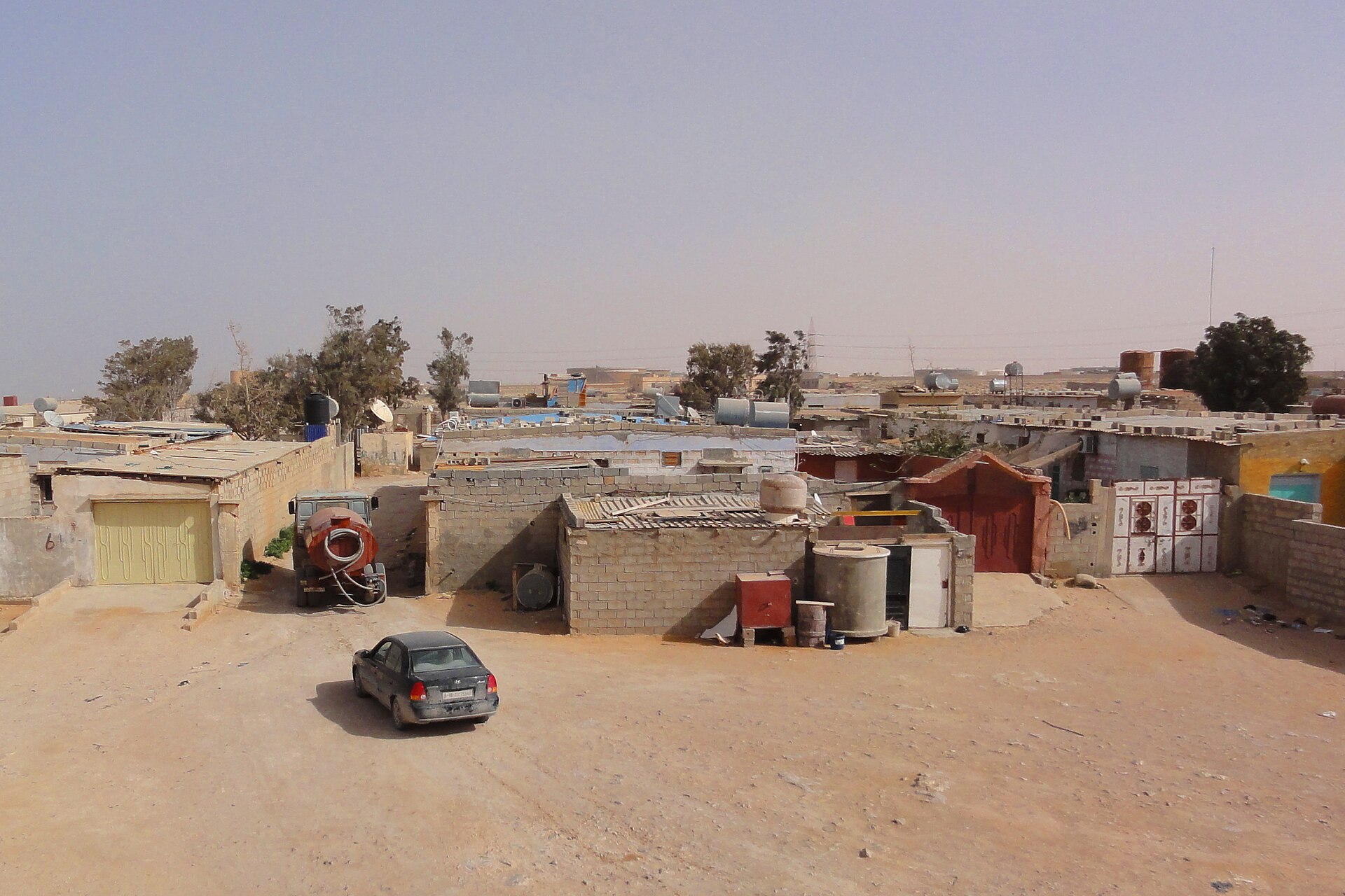Low concrete houses, water tanks and a car on a sandy street in Tobruk