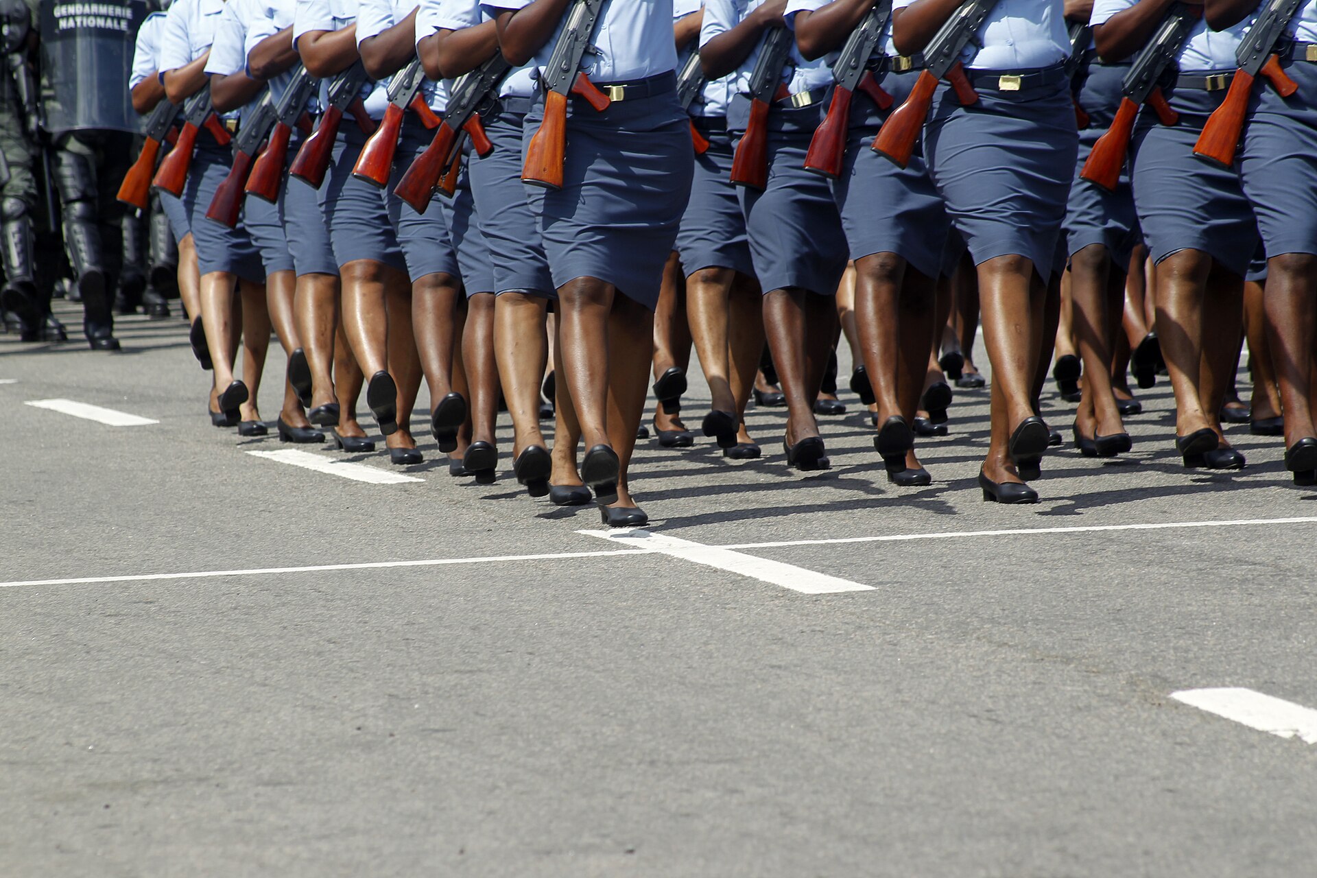 Uniformed Cameroonian gendarmes in light-blue shirts and grey skirts marching with rifles, a Gendarmerie Nationale shield visible at left