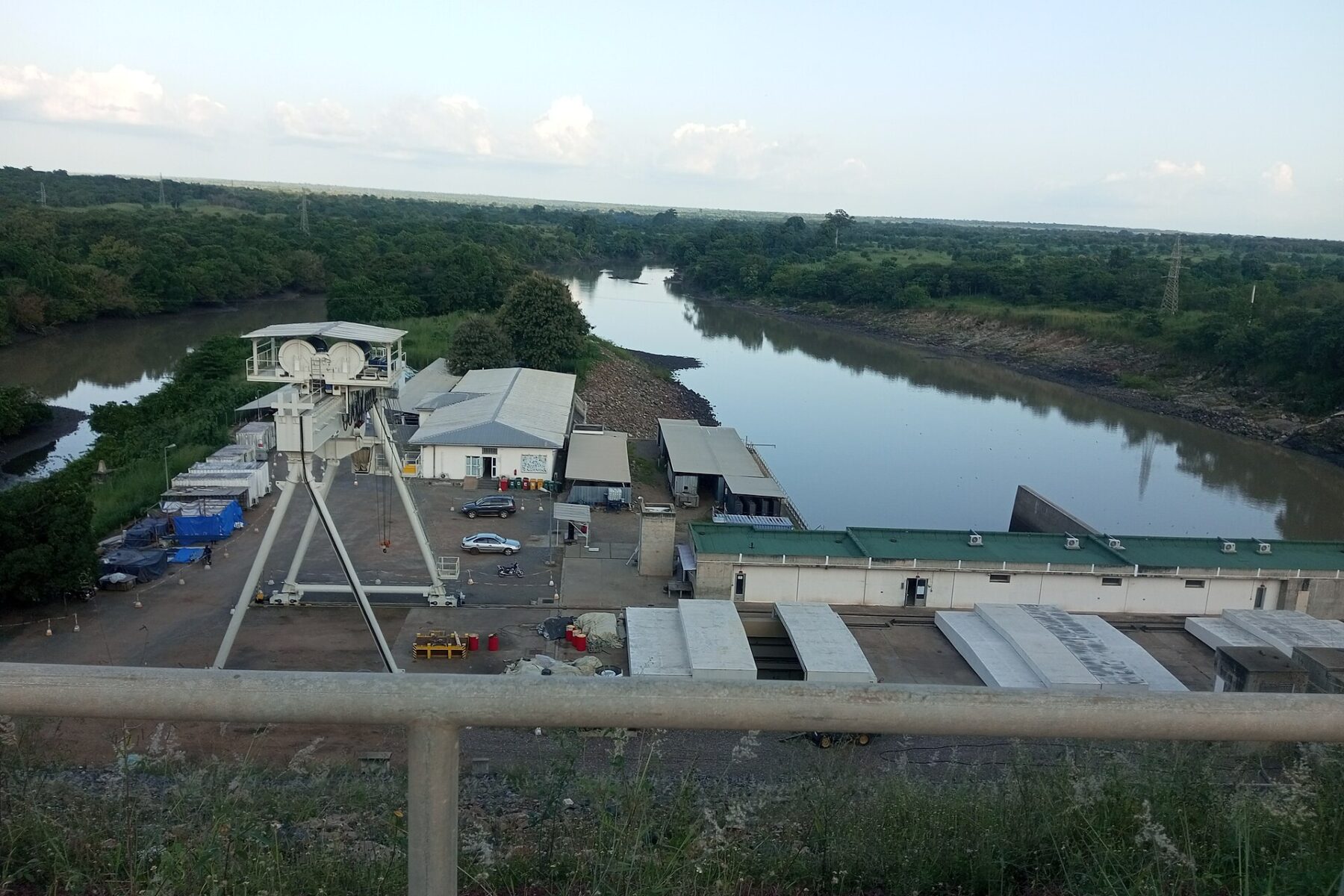 Powerhouse buildings and a gantry crane below the Nangbéto hydroelectric dam in Togo, with the Mono River and green bush behind