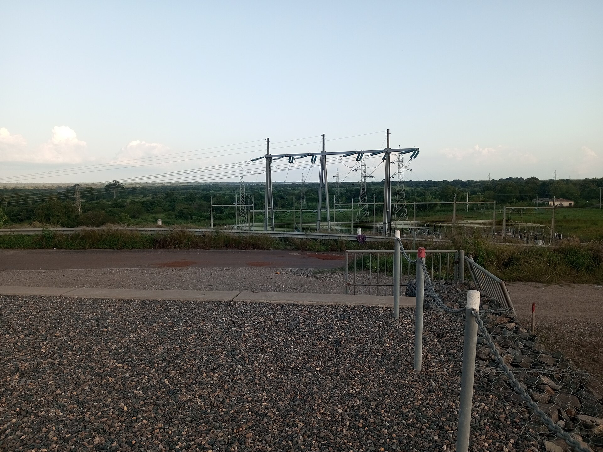High-voltage transmission pylons and lines above a substation at the Nangbéto dam site, with green bush behind