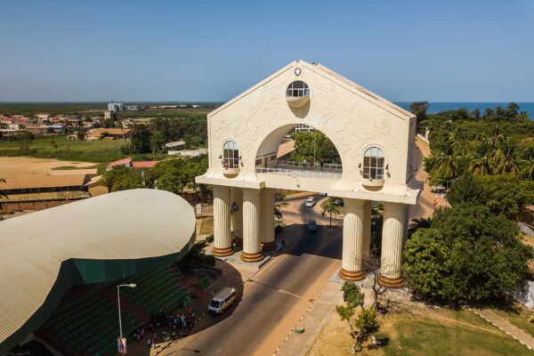 Aerial view of Arch 22, a white monumental gateway over the main road into Banjul, with the Atlantic Ocean behind
