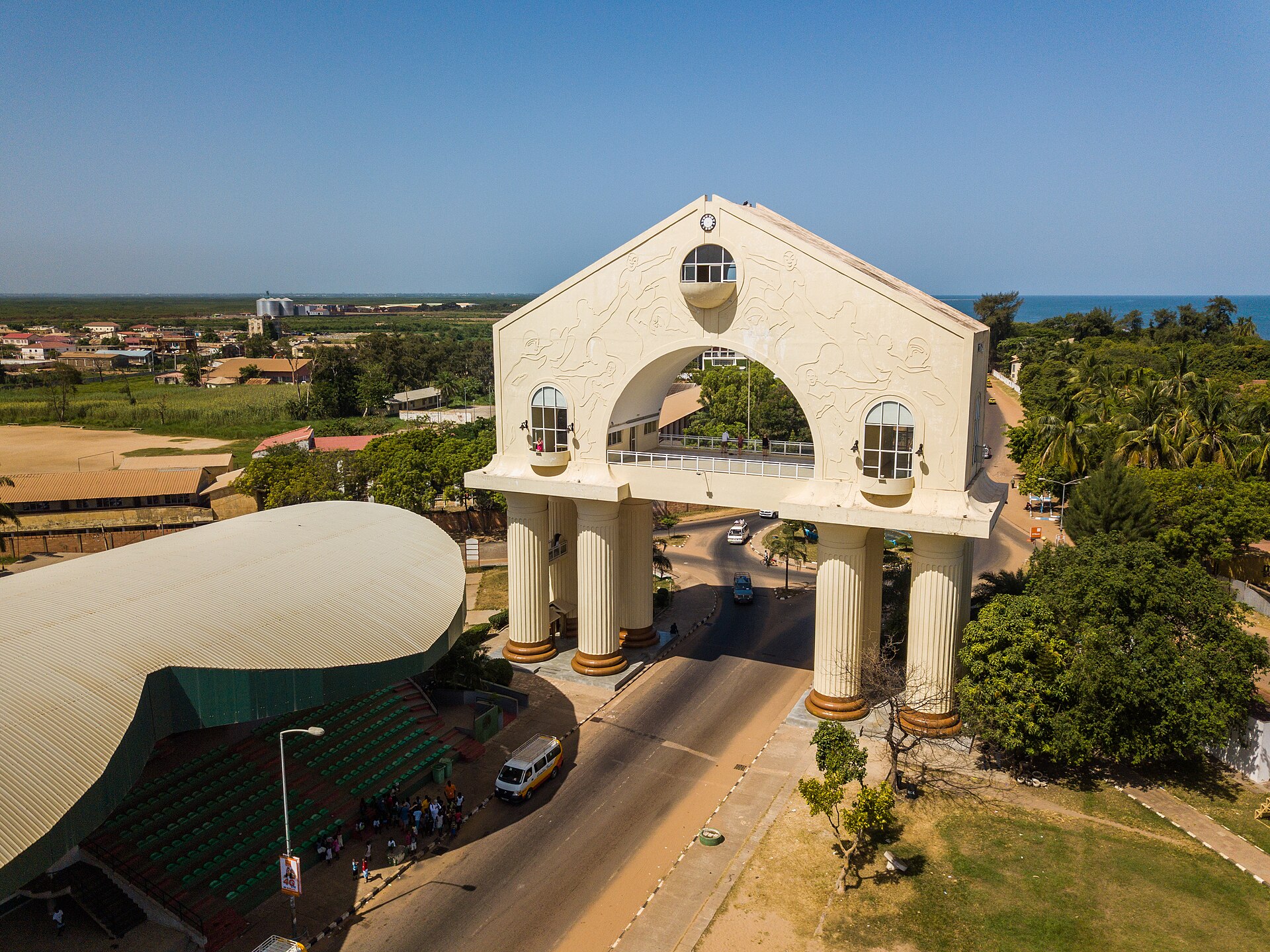Aerial view of Arch 22, a white monumental gateway over the main road into Banjul, with the Atlantic Ocean behind