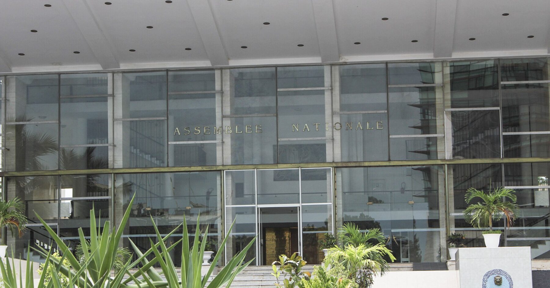 Glass facade of the National Assembly building in Dakar with the words Assemblee Nationale above the entrance and palm plants in front