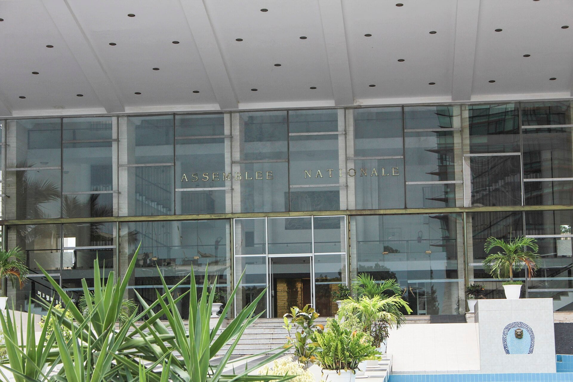 Glass facade of the National Assembly building in Dakar with the words Assemblee Nationale above the entrance and palm plants in front