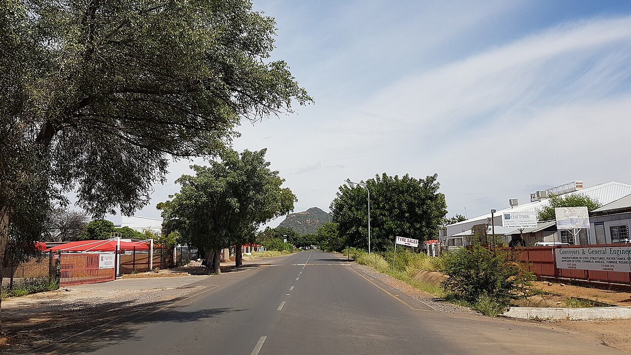 A quiet road in Gaborone's industrial area with workshops, tree shade and a hill in the distance