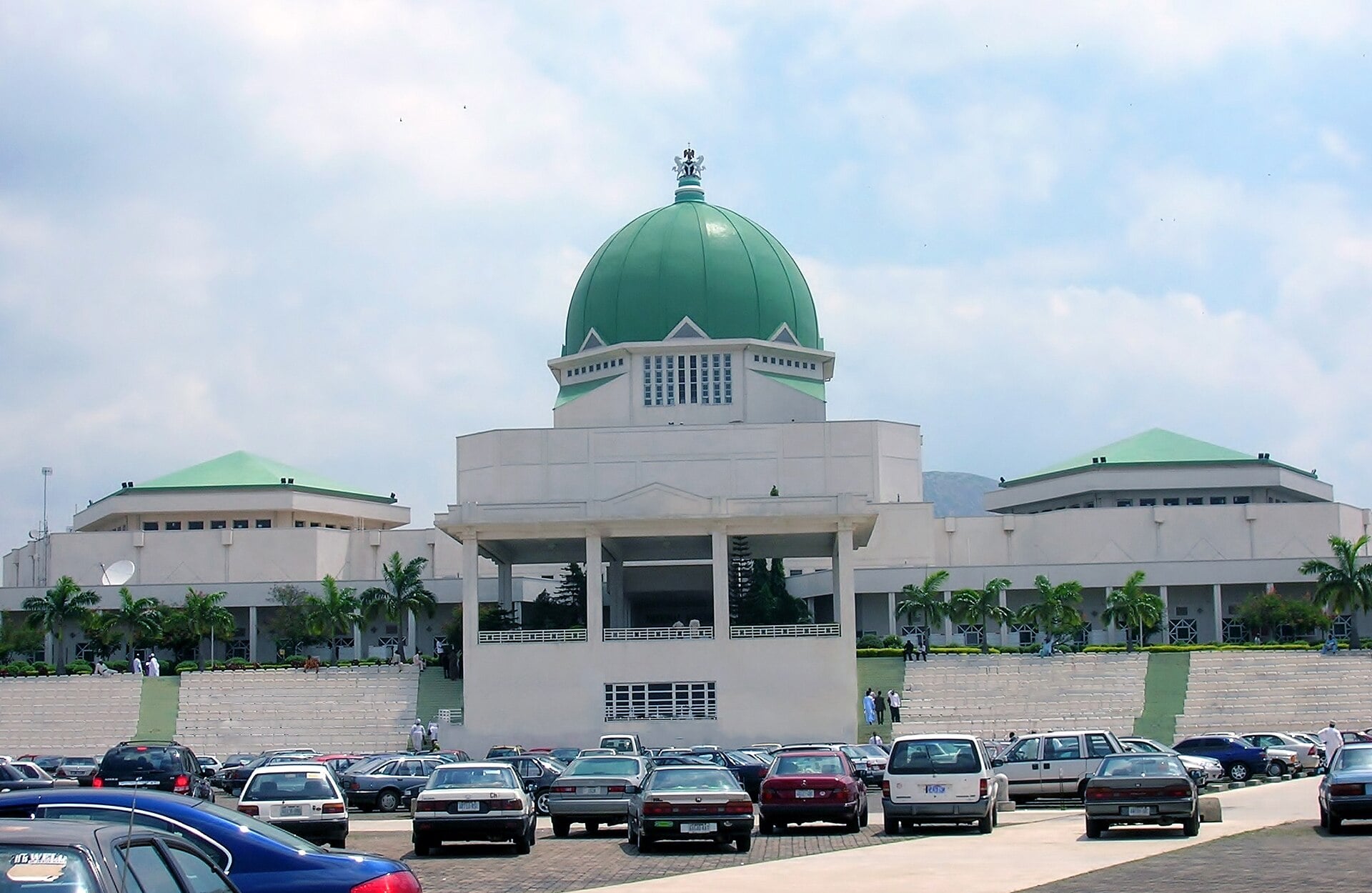 White National Assembly complex with a green dome in Abuja, Nigeria, behind a car park