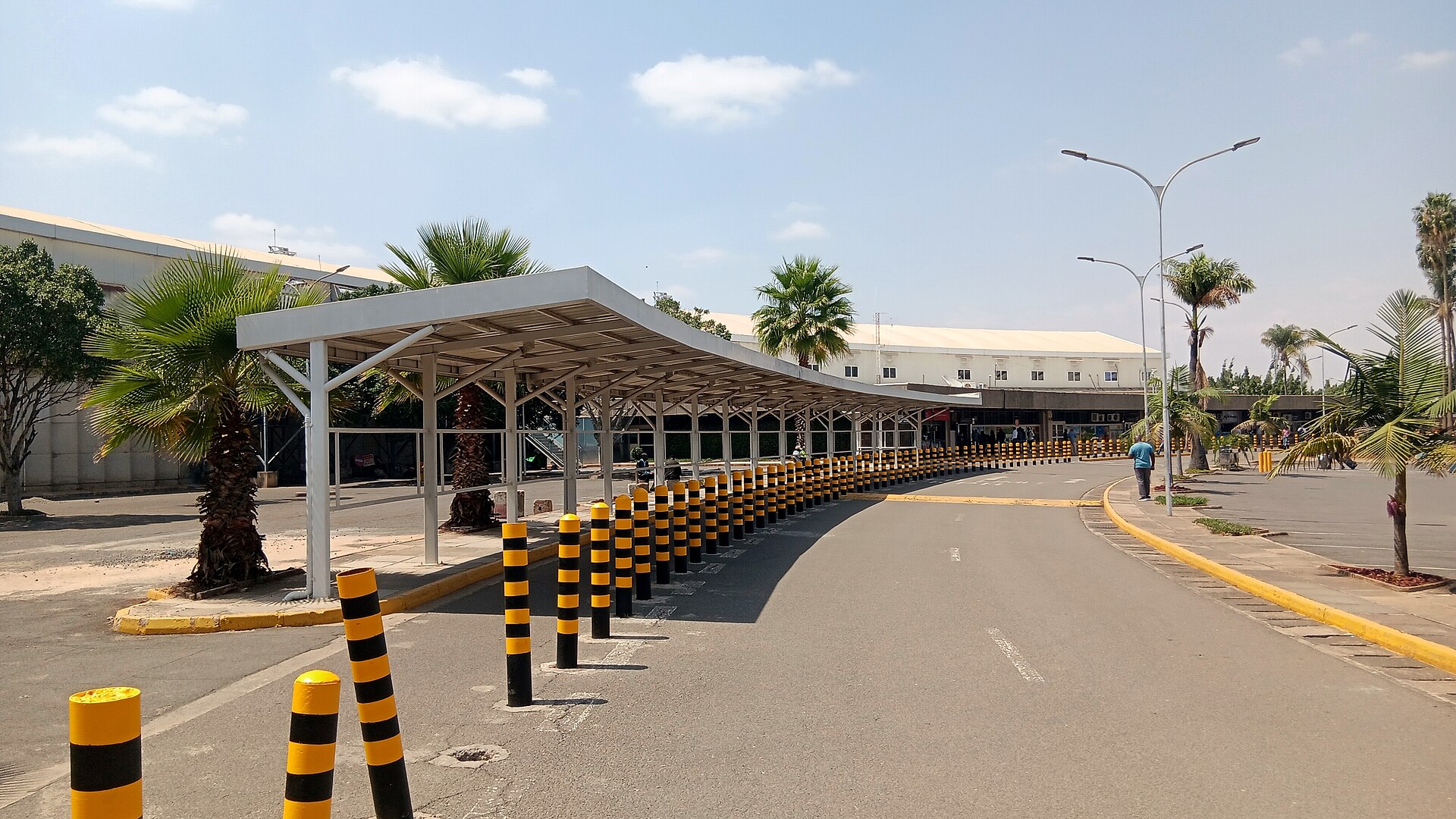 A covered walkway lined with yellow-and-black bollards beside the terminal building of Jomo Kenyatta International Airport in Nairobi