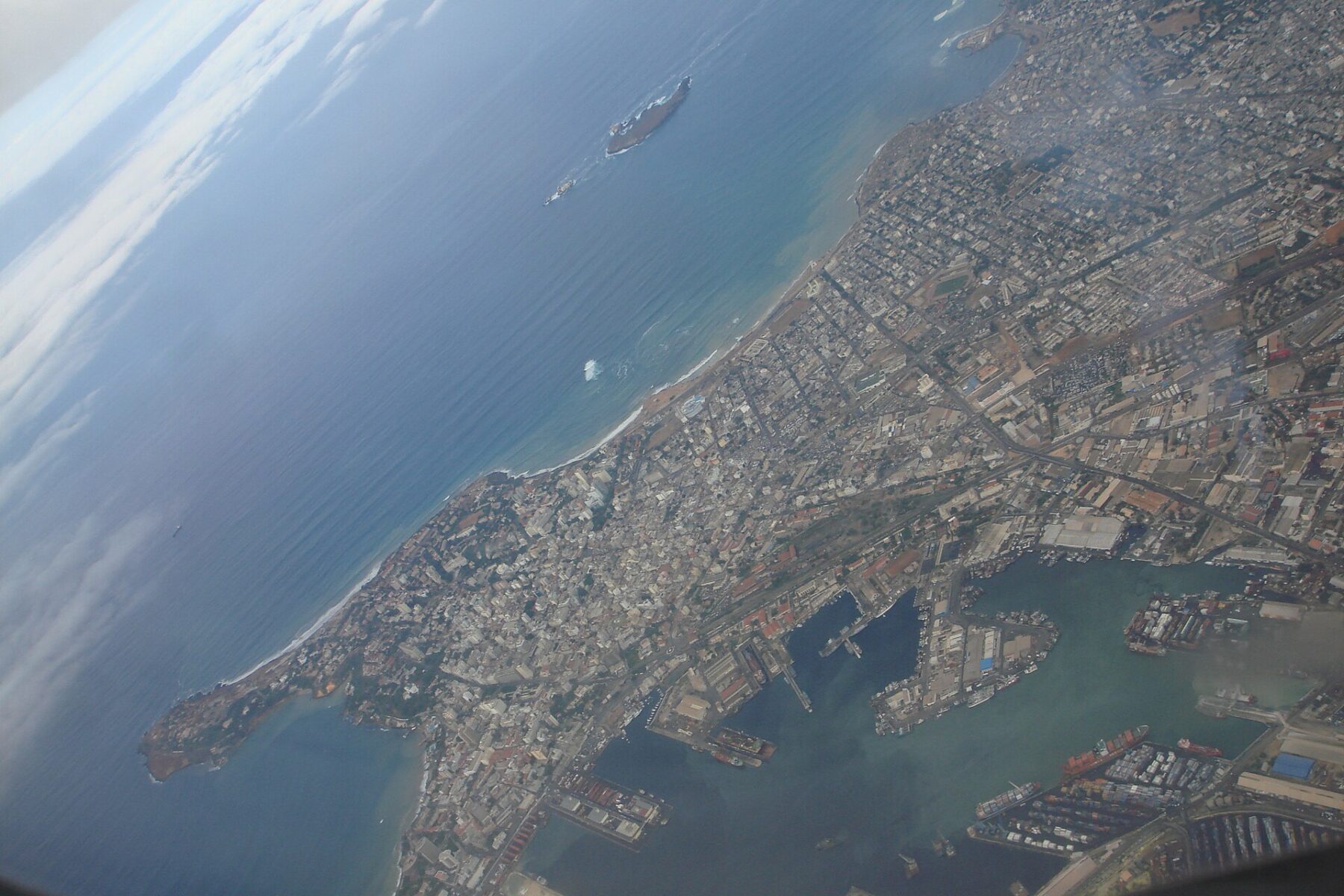 Aerial view of Dakar's harbour with cranes, ships at the quays, dense city blocks and the Atlantic coast, taken from an aircraft window