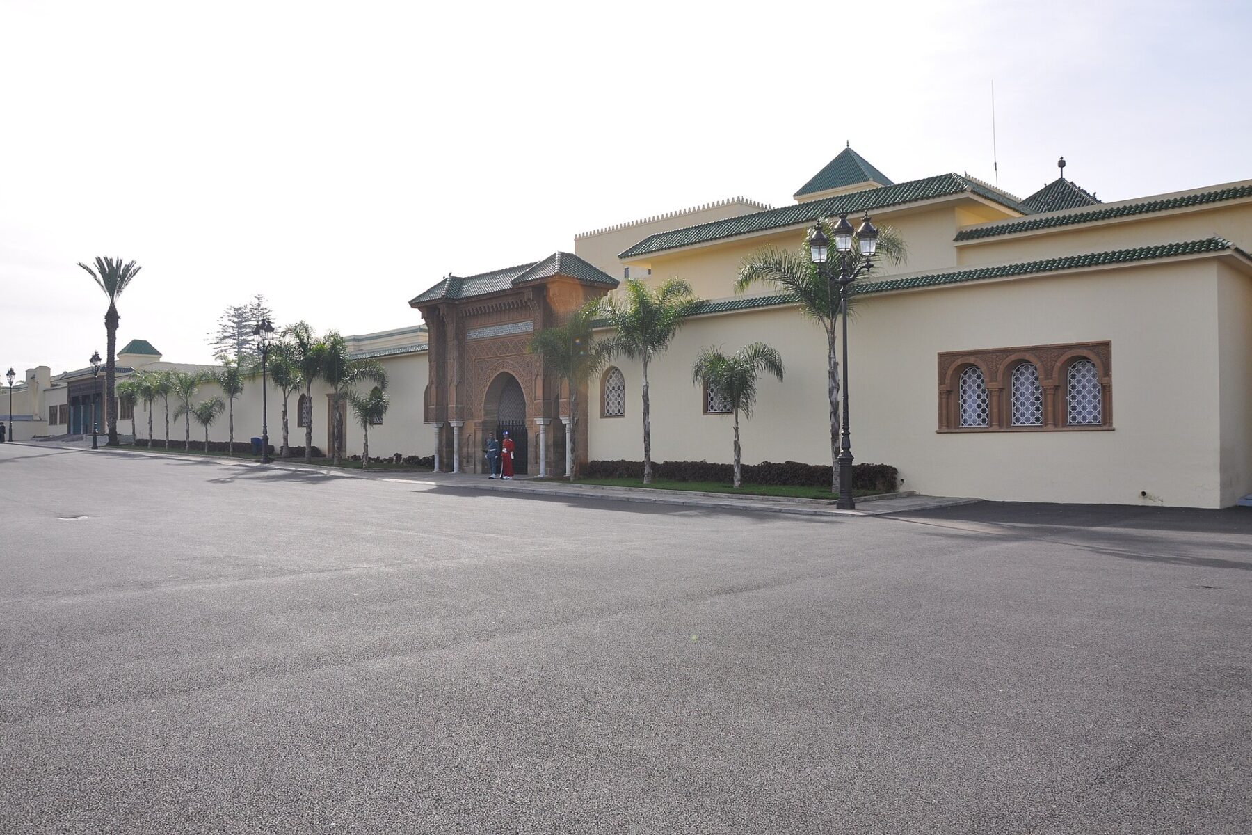 The Royal Palace in Rabat, a cream-walled Moroccan palace with a tiled gate, palm trees and an empty paved square.